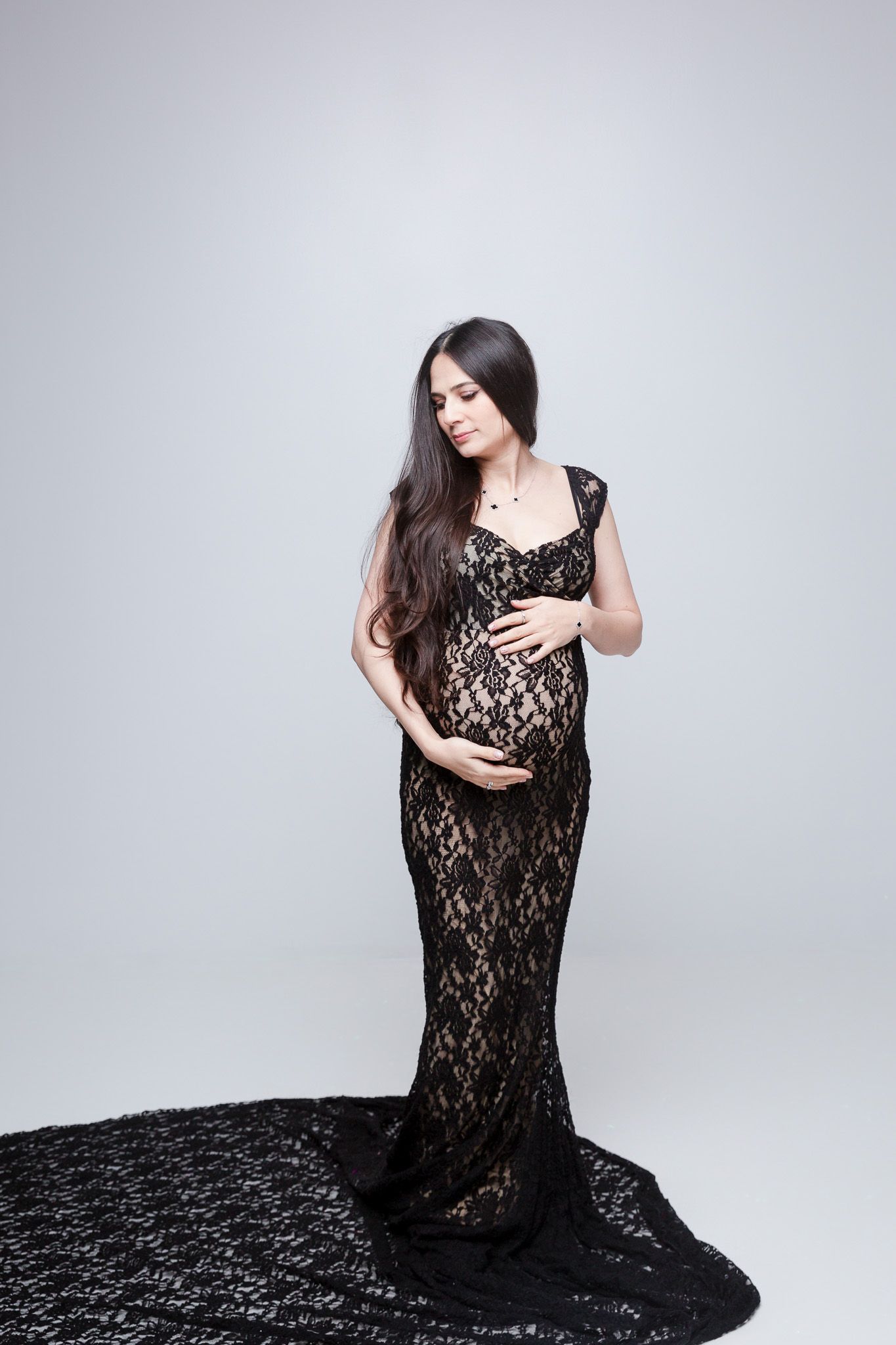 Elegant maternity photo shoot featuring a flowing black lace gown against a light backdrop.