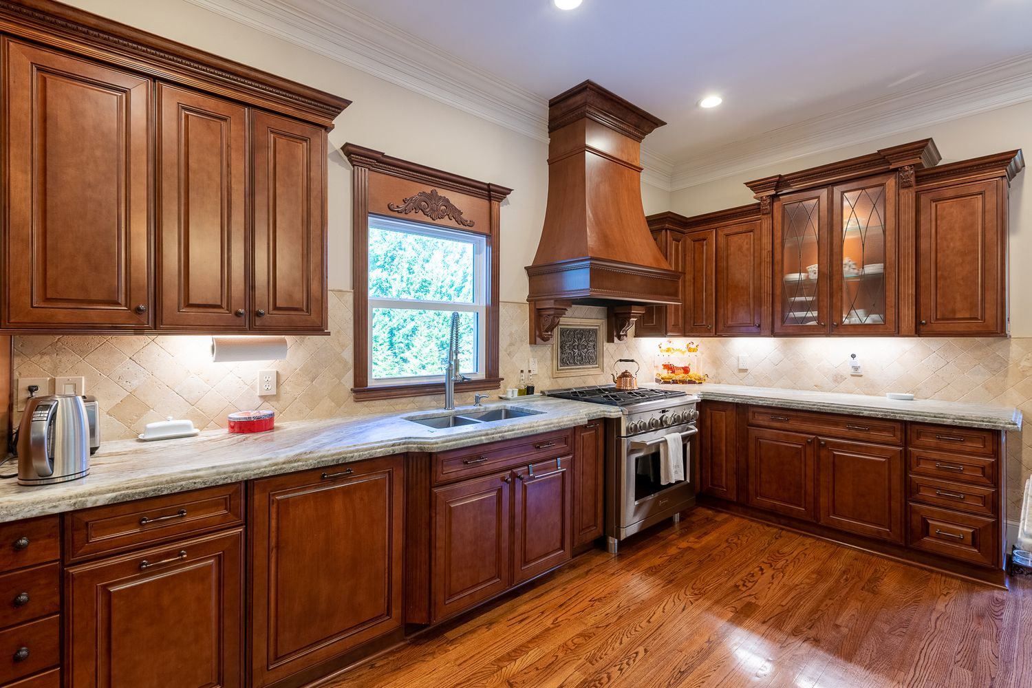 Modern kitchen featuring cherry wood cabinets, crown molding, and recessed lighting in wide panoramic view.