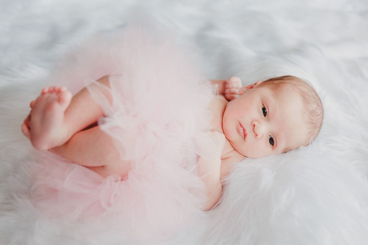 Delicate newborn portrait series on white textured background with soft pink tones.