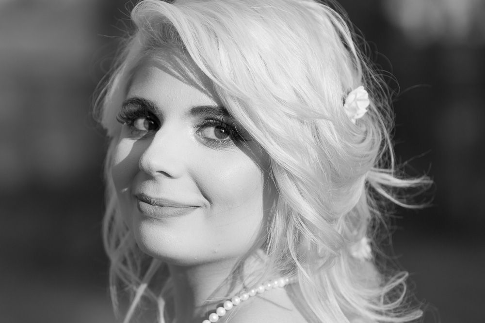 Elegant blonde bride wearing pearl necklace and hair accessory in a classic black and white portrait.
