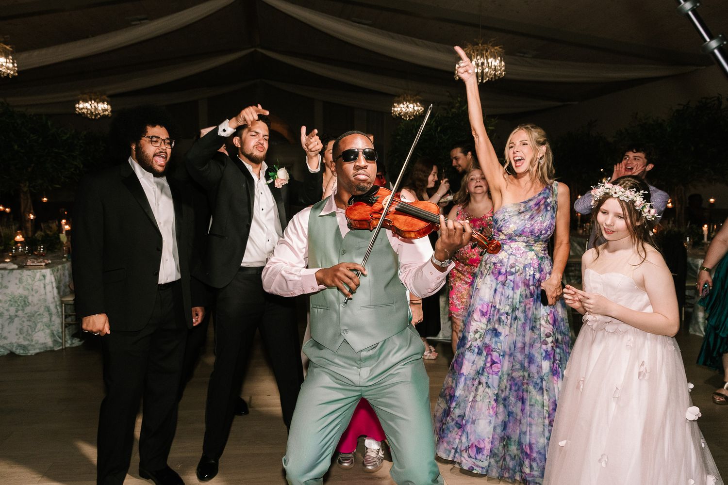 Violinist entertains wedding guests as bridal party dances with sparklers at reception.