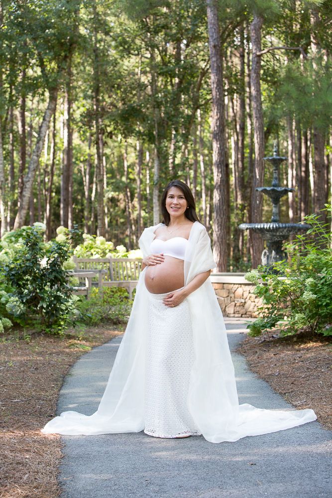 Artistic maternity portraits in wooded park setting with decorative fountain in background.
