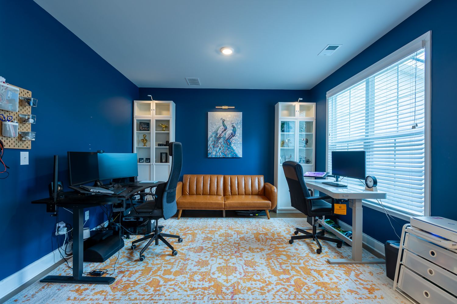 Modern home office with deep blue walls, built-in shelving, and yellow accent furniture.