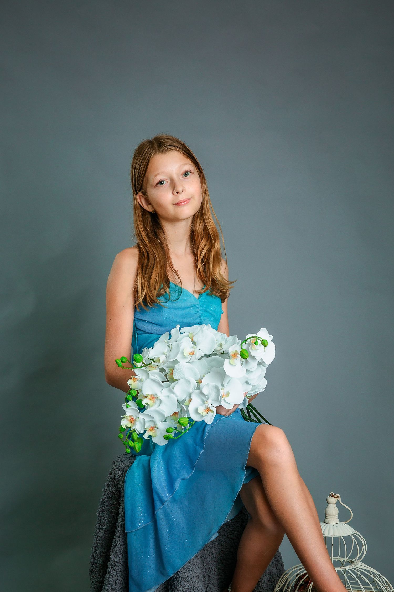 Studio portrait session featuring blue dress and white orchids against grey backdrop.