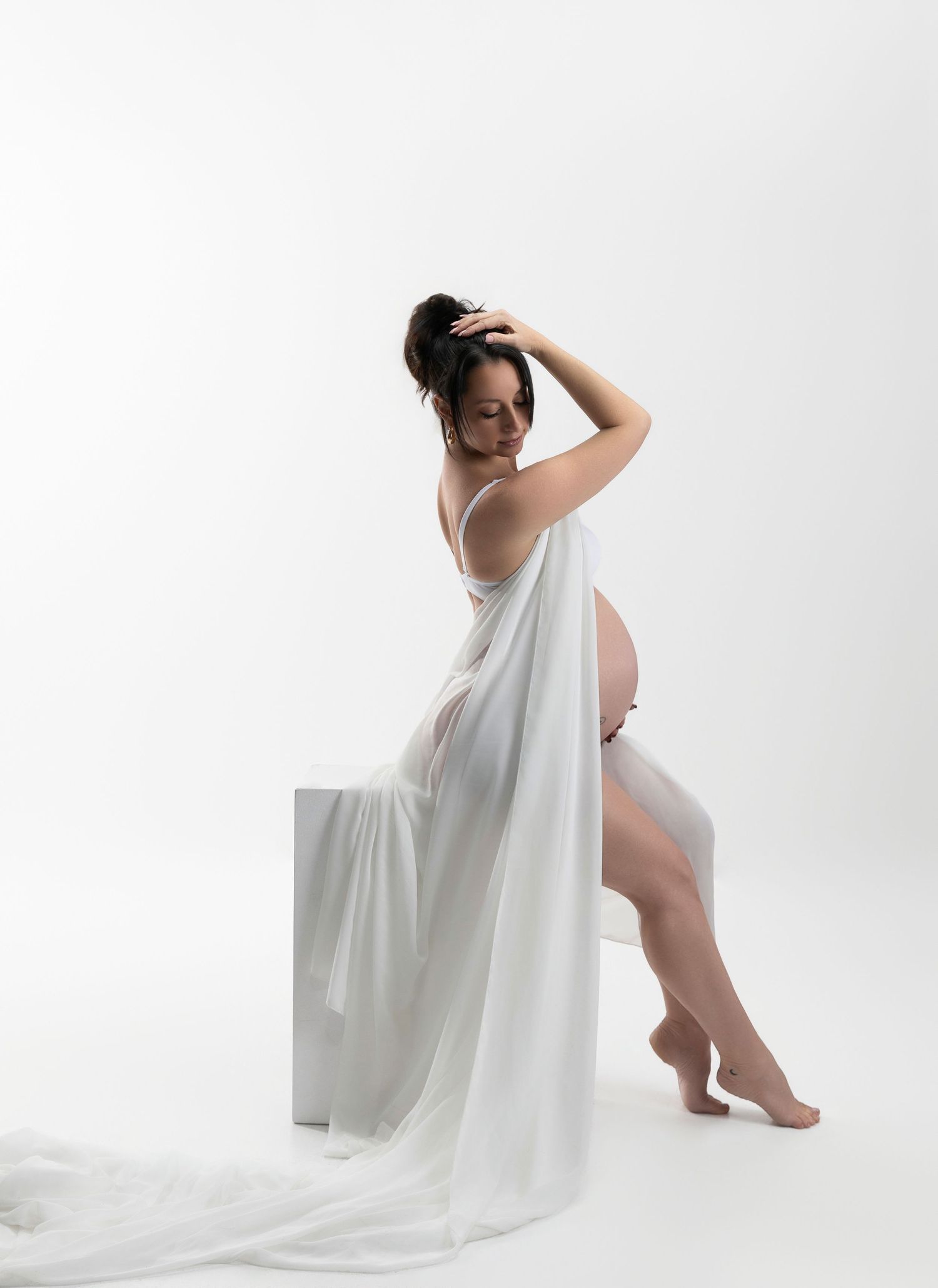 Ethereal maternity portrait with flowing white fabric against bright studio background.