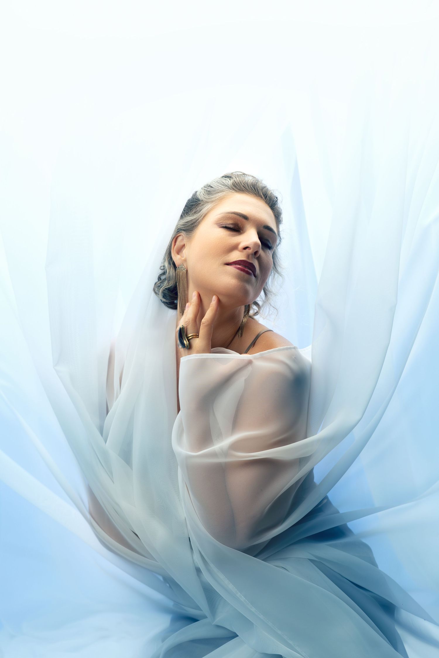 Ethereal portrait with flowing sheer fabric in soft blue and white tones creating a dreamy atmosphere.