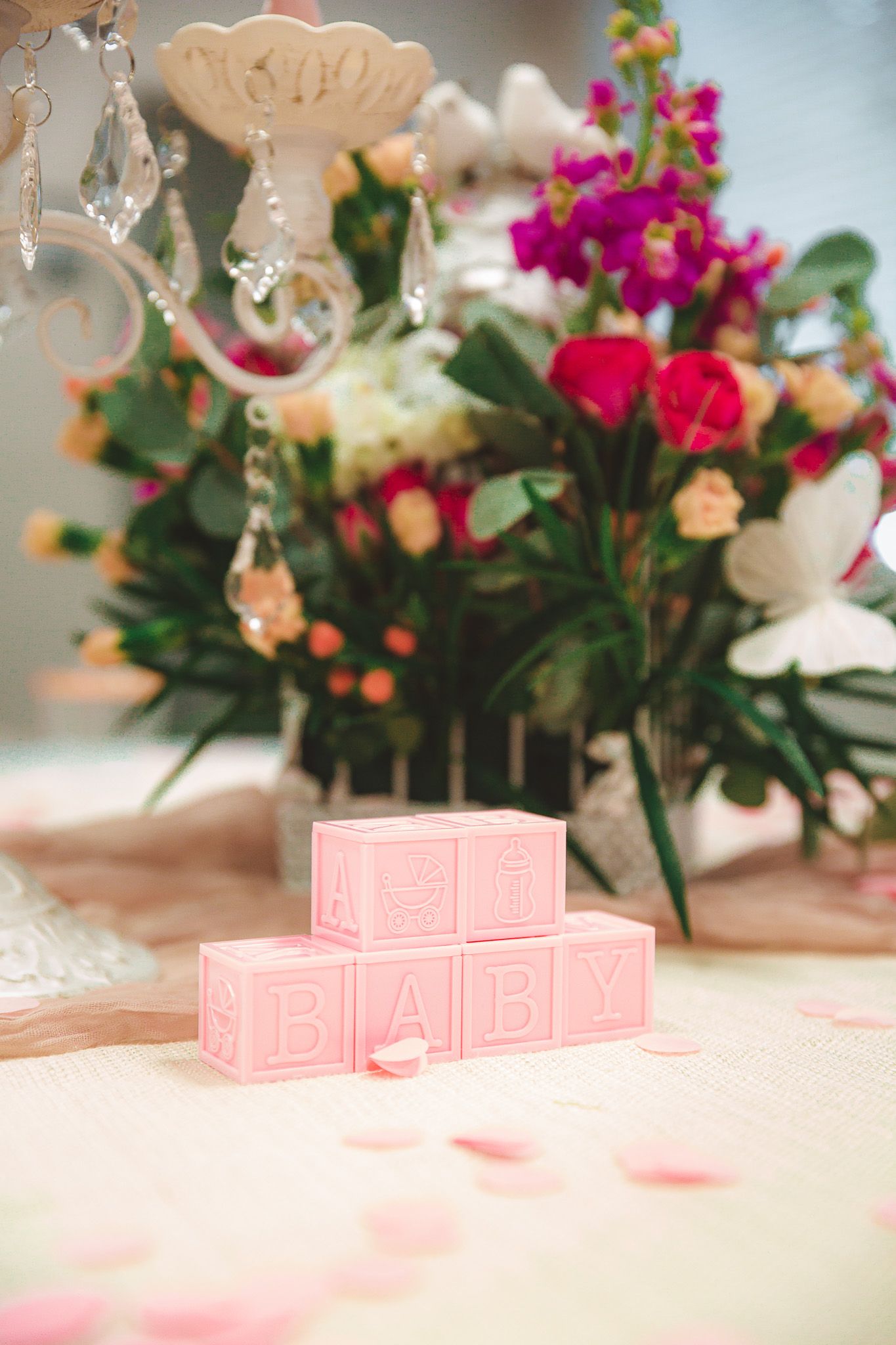 Pink decorative blocks arranged on white tablecloth with colorful floral arrangements in background.