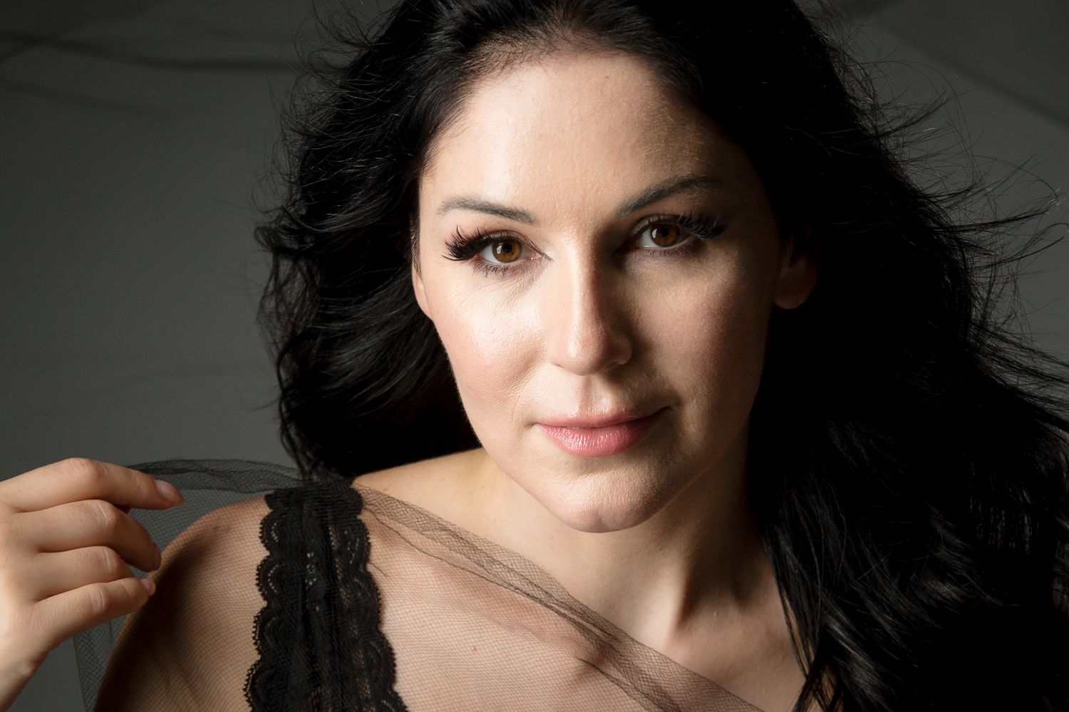 Close up beauty portrait with dark hair and natural makeup against light background.