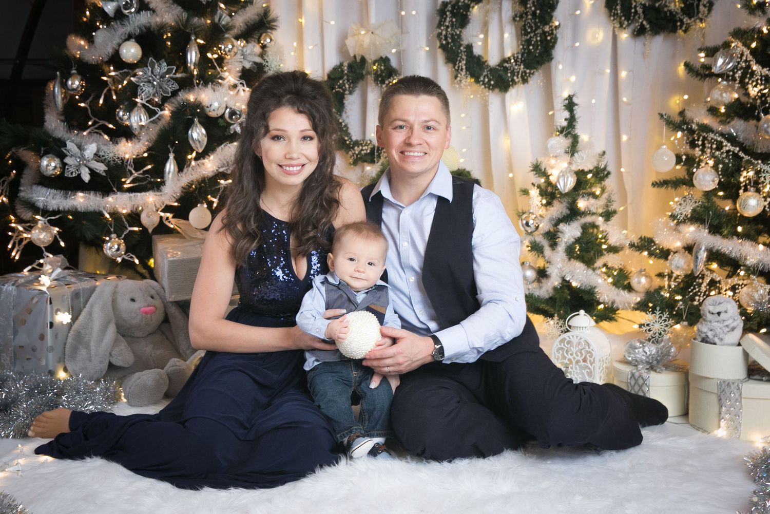 Holiday family portrait with Christmas trees and white decorations creating a warm atmosphere.