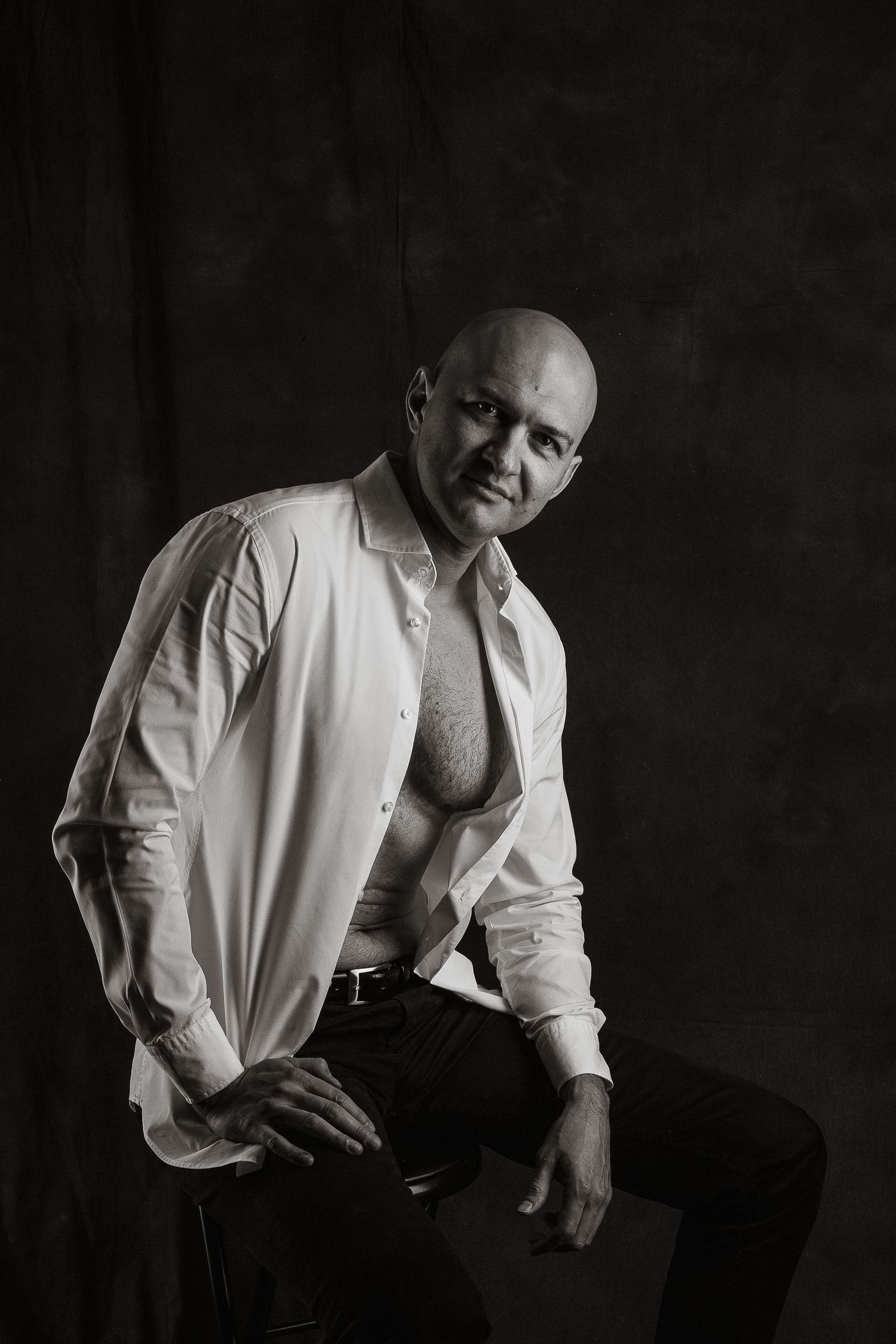 Dramatic black and white portrait of a muscular man in an unbuttoned white shirt.