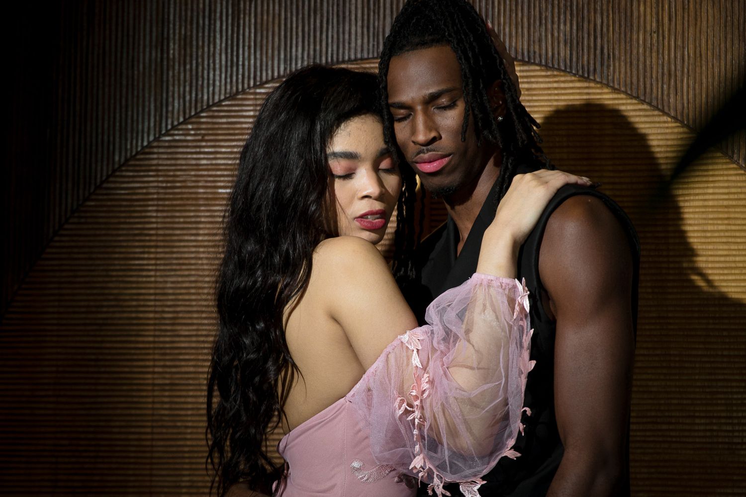 A romantic couple embraces intimately in moody lighting with warm brown tones in the background.
