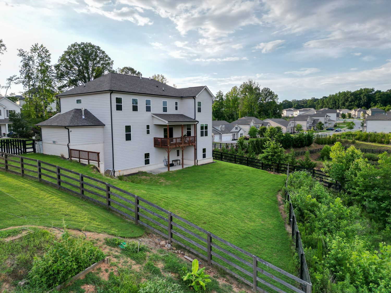 Aerial perspective of residential properties with black rail fencing and lush green surroundings.