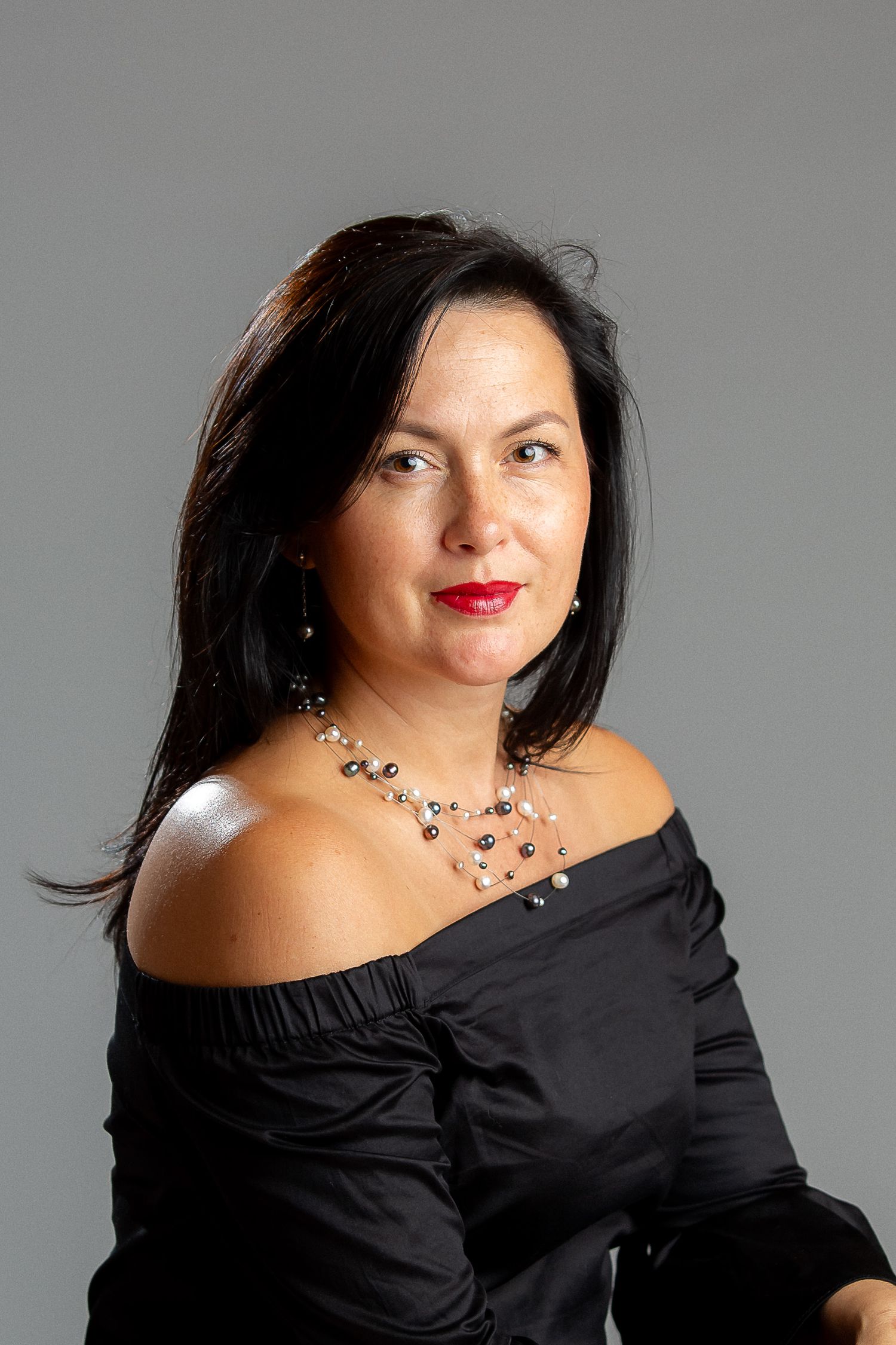 Elegant portrait in black off-shoulder dress against gray backdrop.