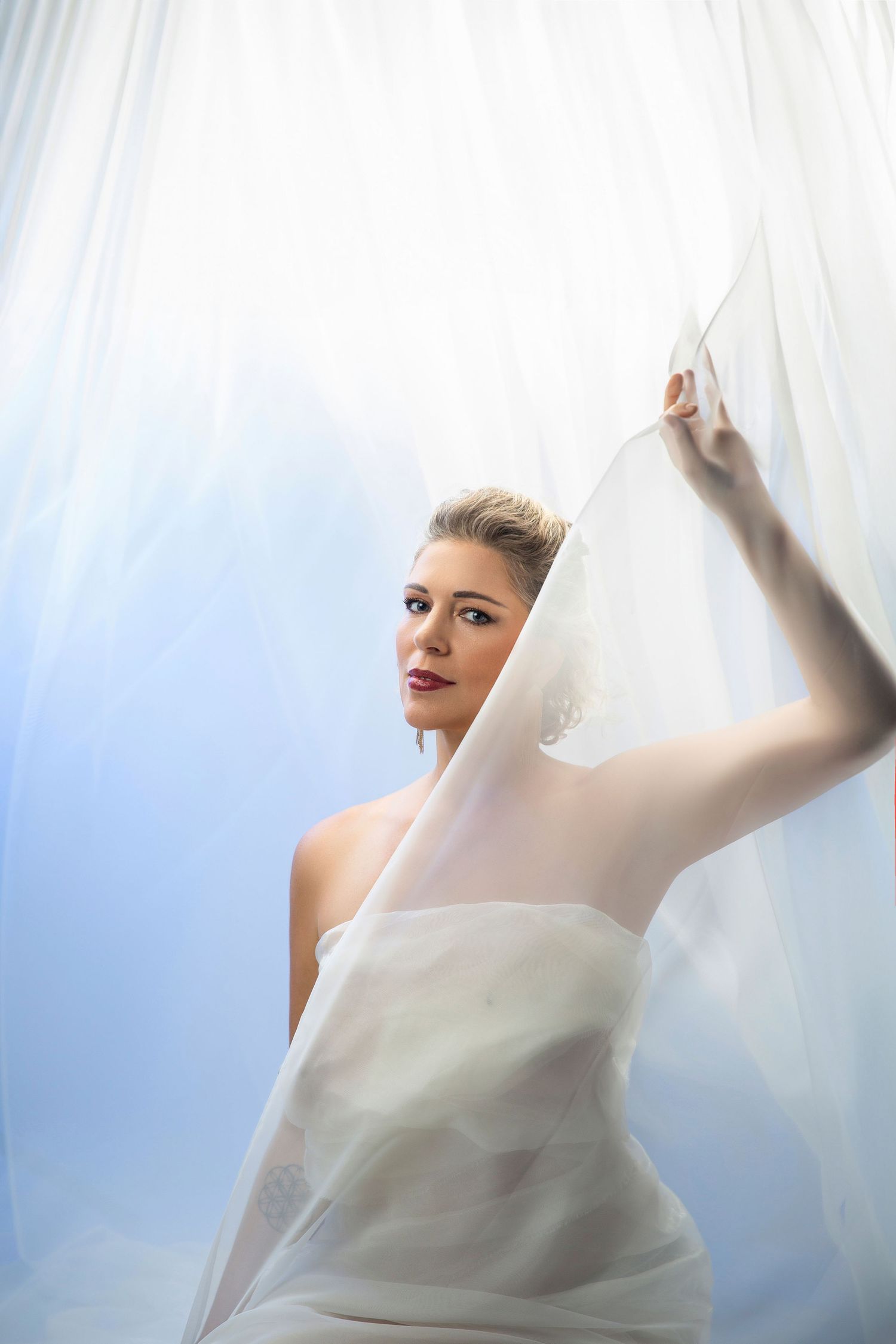Elegant bridal portrait with flowing white fabric and soft lighting creating an ethereal mood.
