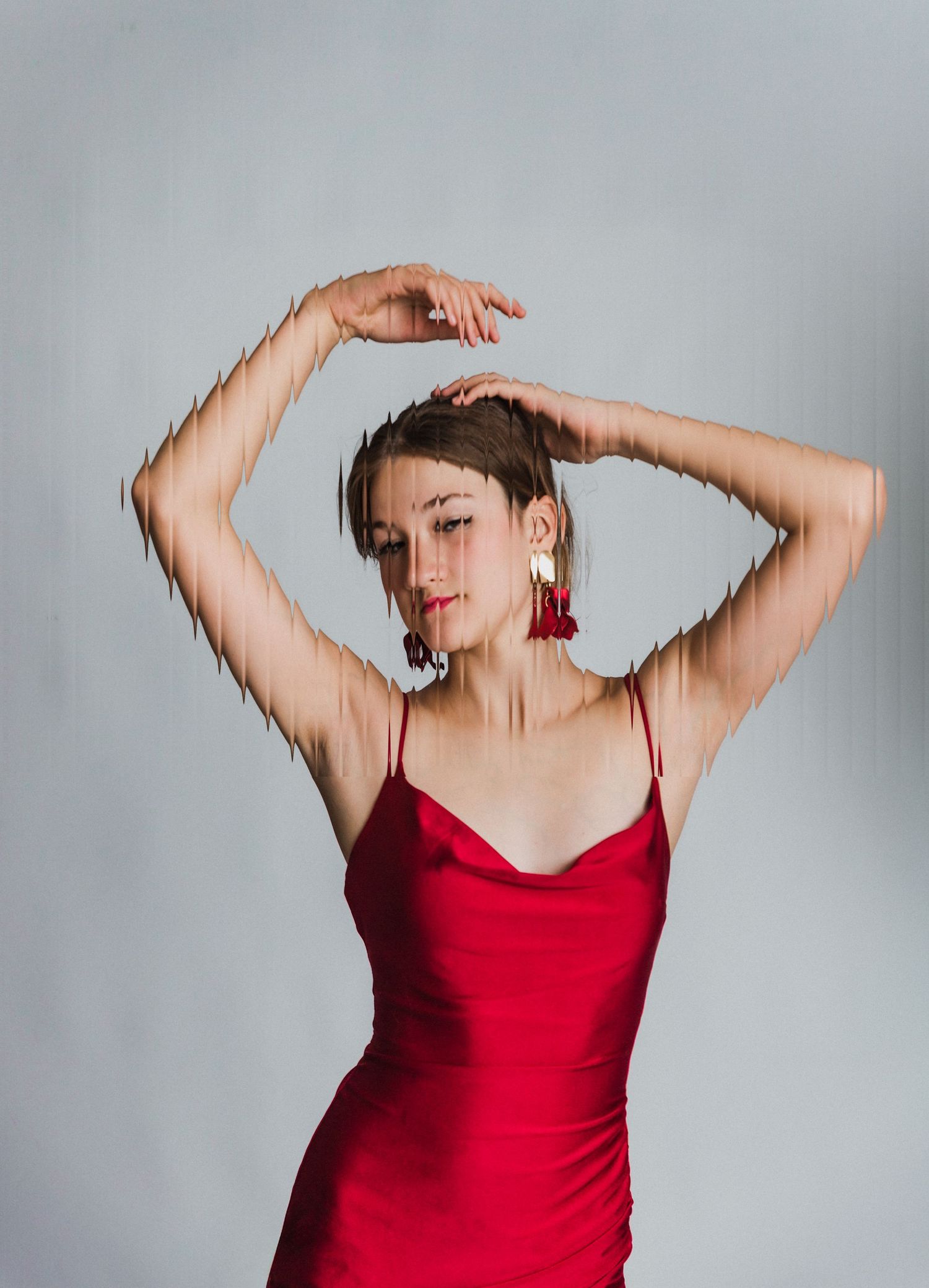A dancer in a red dress poses gracefully with raised arms against a light gray background.