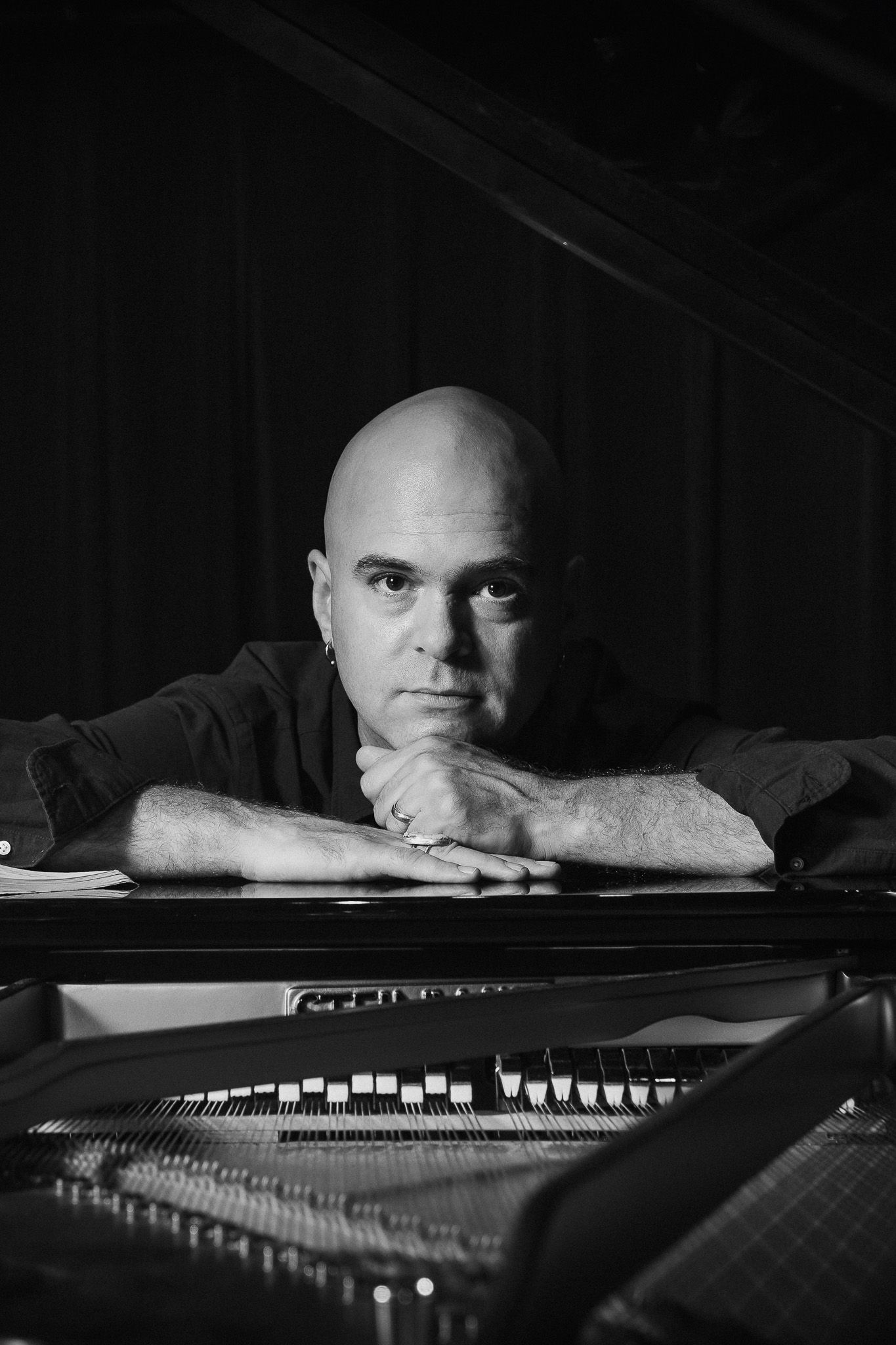 Artistic black and white photo of a musician resting on a grand piano.