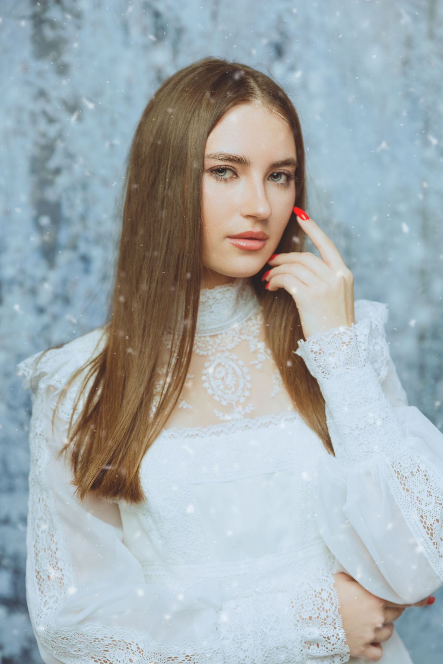 Ethereal winter portrait in delicate white lace dress against blue backdrop.