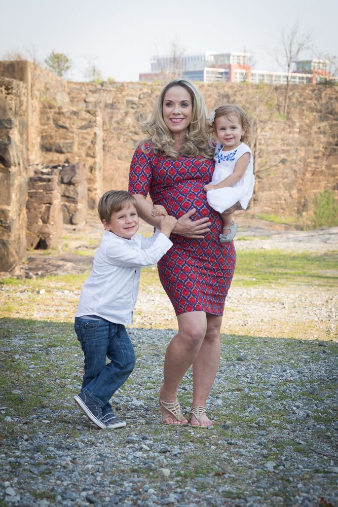 Playful family maternity photo session outdoors with stone wall backdrop and natural lighting.