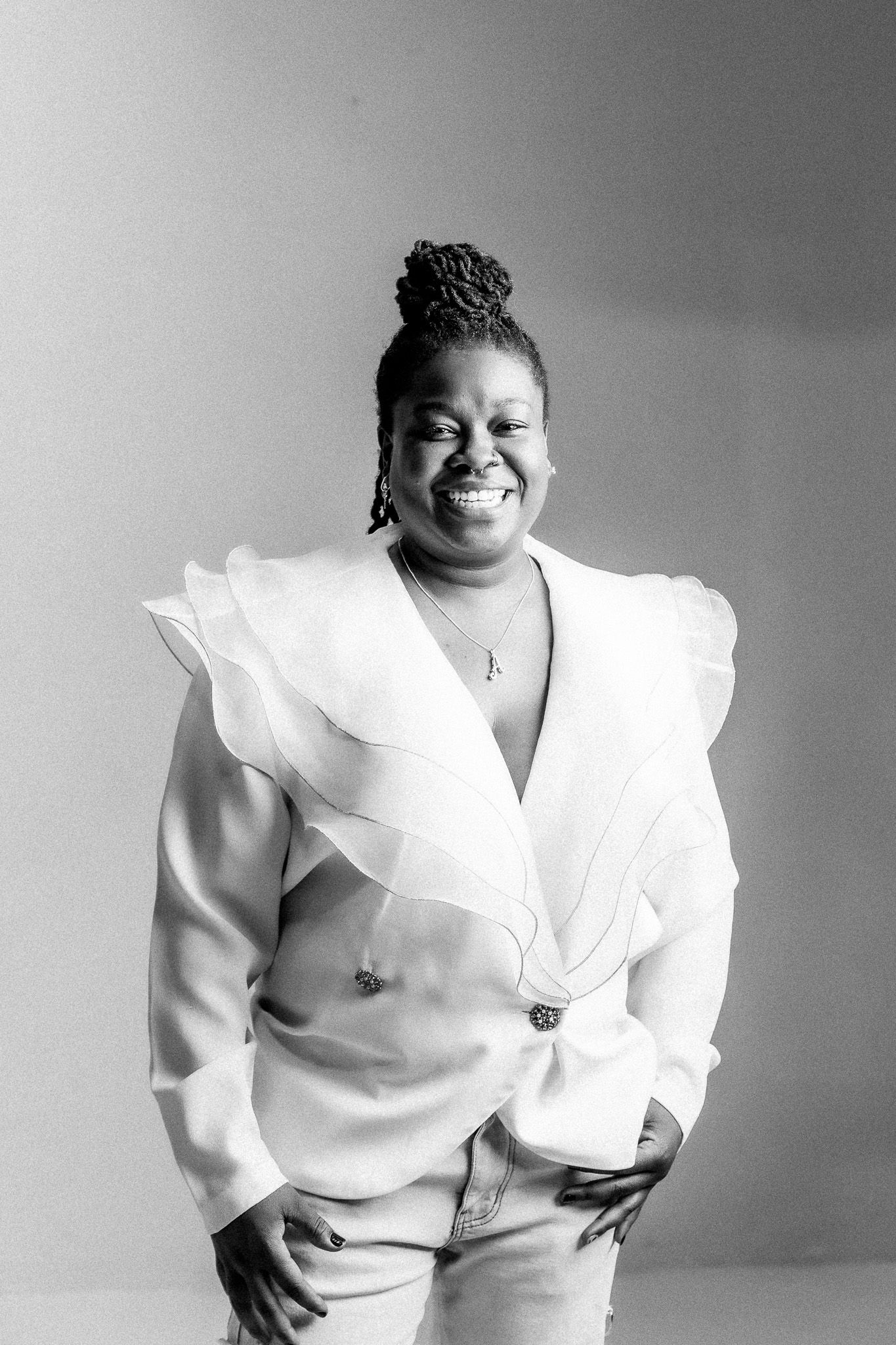 Black and white portrait featuring bright smile and stylish white ruffled blazer.