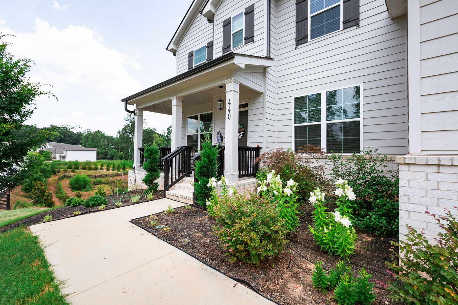 Front entrance of a white house with covered porch and landscaped garden beds.