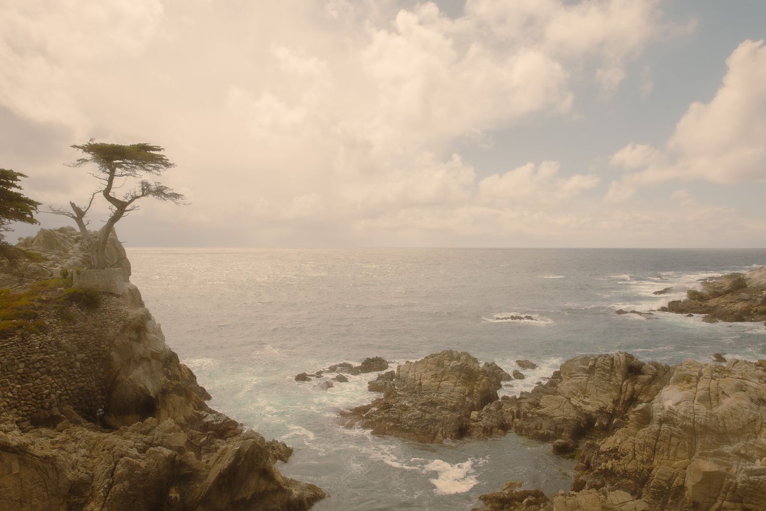 Dramatic coastal landscape with rocky cliffs and crashing waves under cloudy skies.