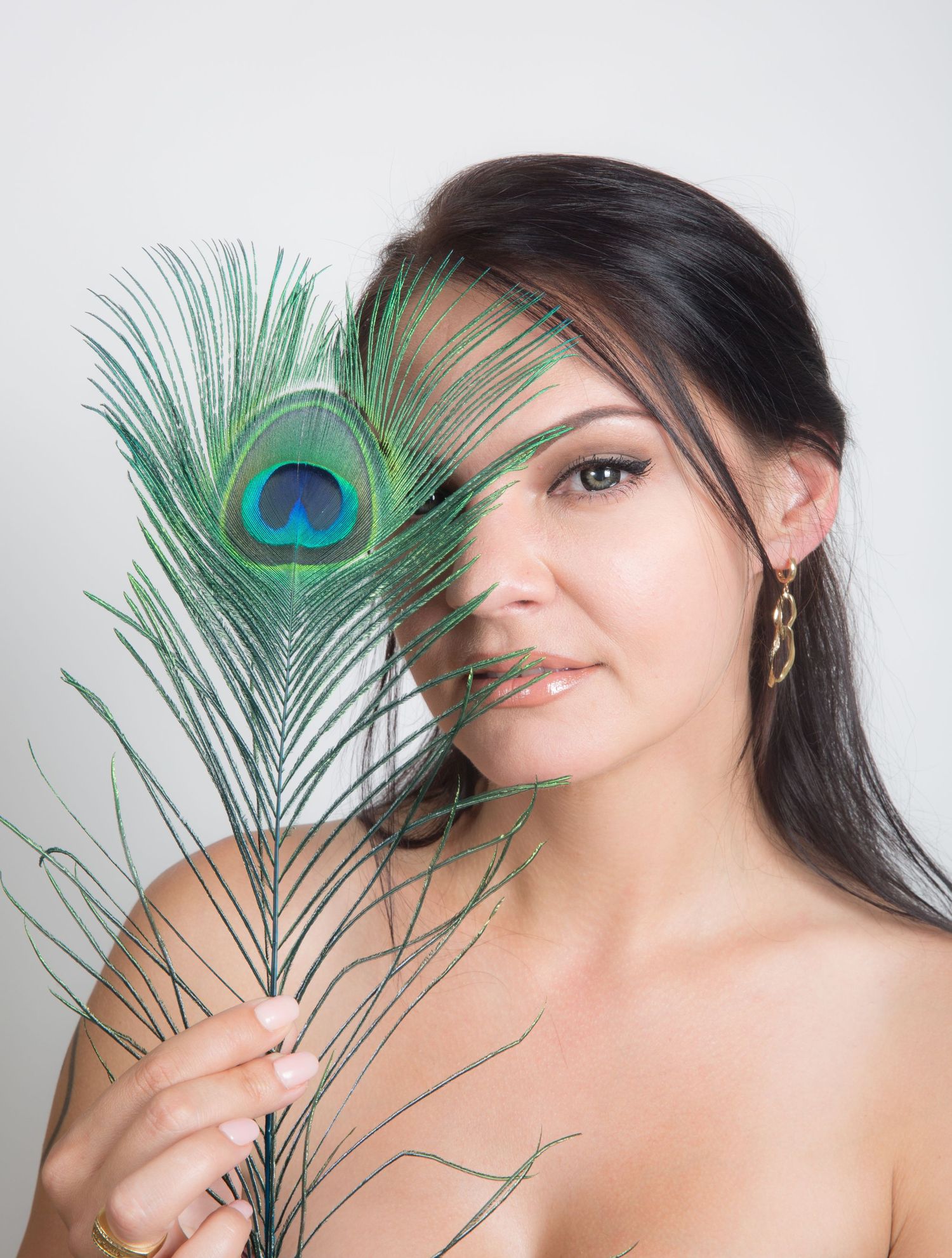 Creative portrait featuring a peacock feather against a light background.