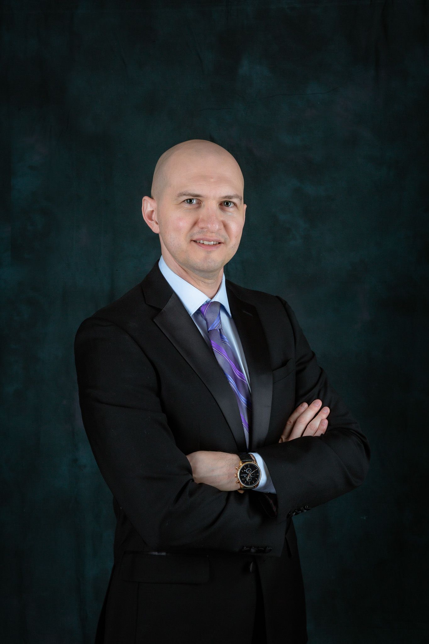 Professional headshots against dark backdrop featuring business attire with purple tie.