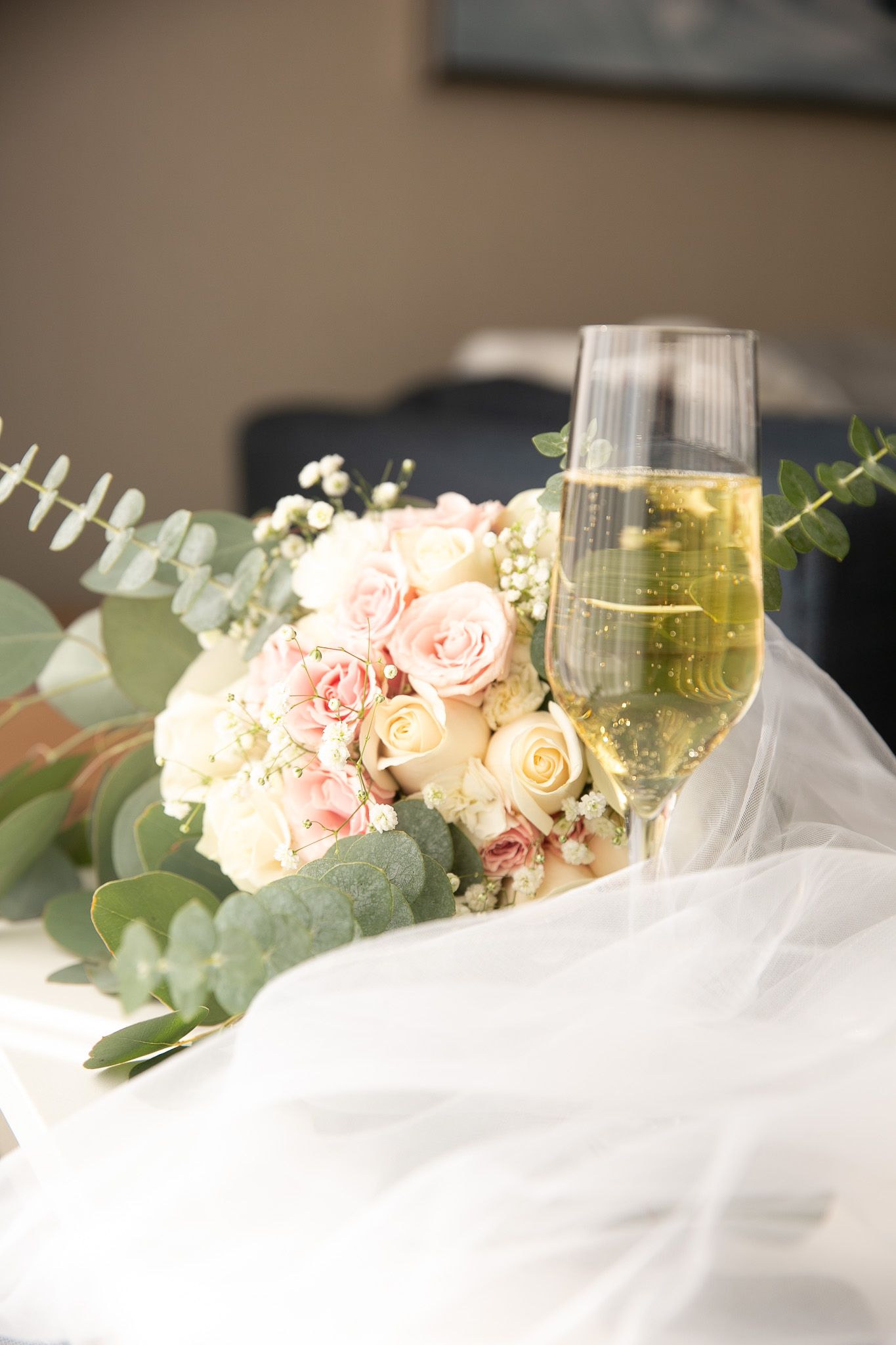 Wedding bouquet of pink and white roses beside champagne flutes on a white veil.