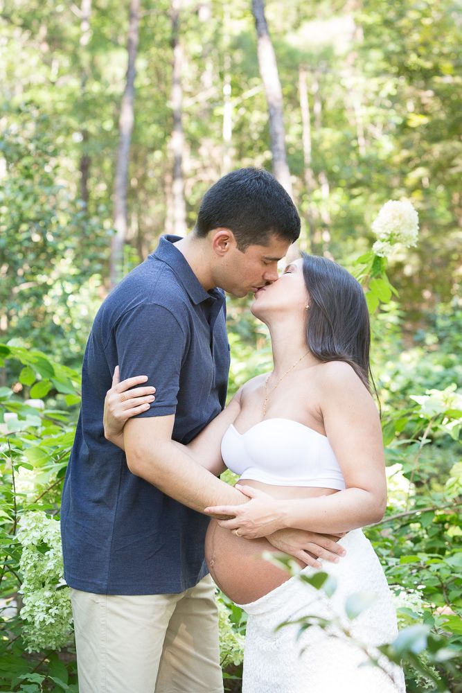 Romantic maternity portraits of a couple sharing intimate moments in a sunlit wooded setting.