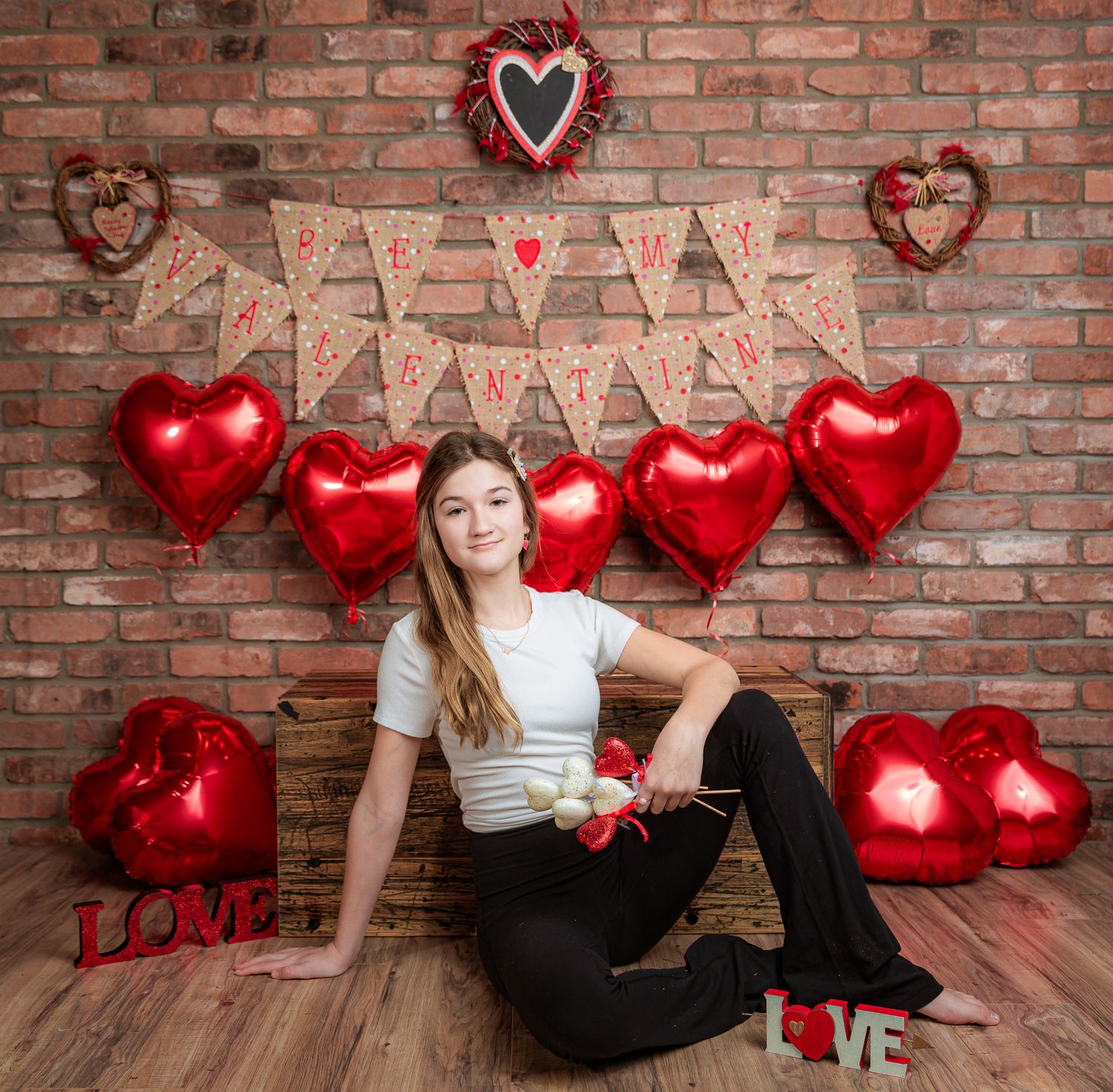 Valentine's themed photoshoot with red heart balloons against rustic brick wall background.