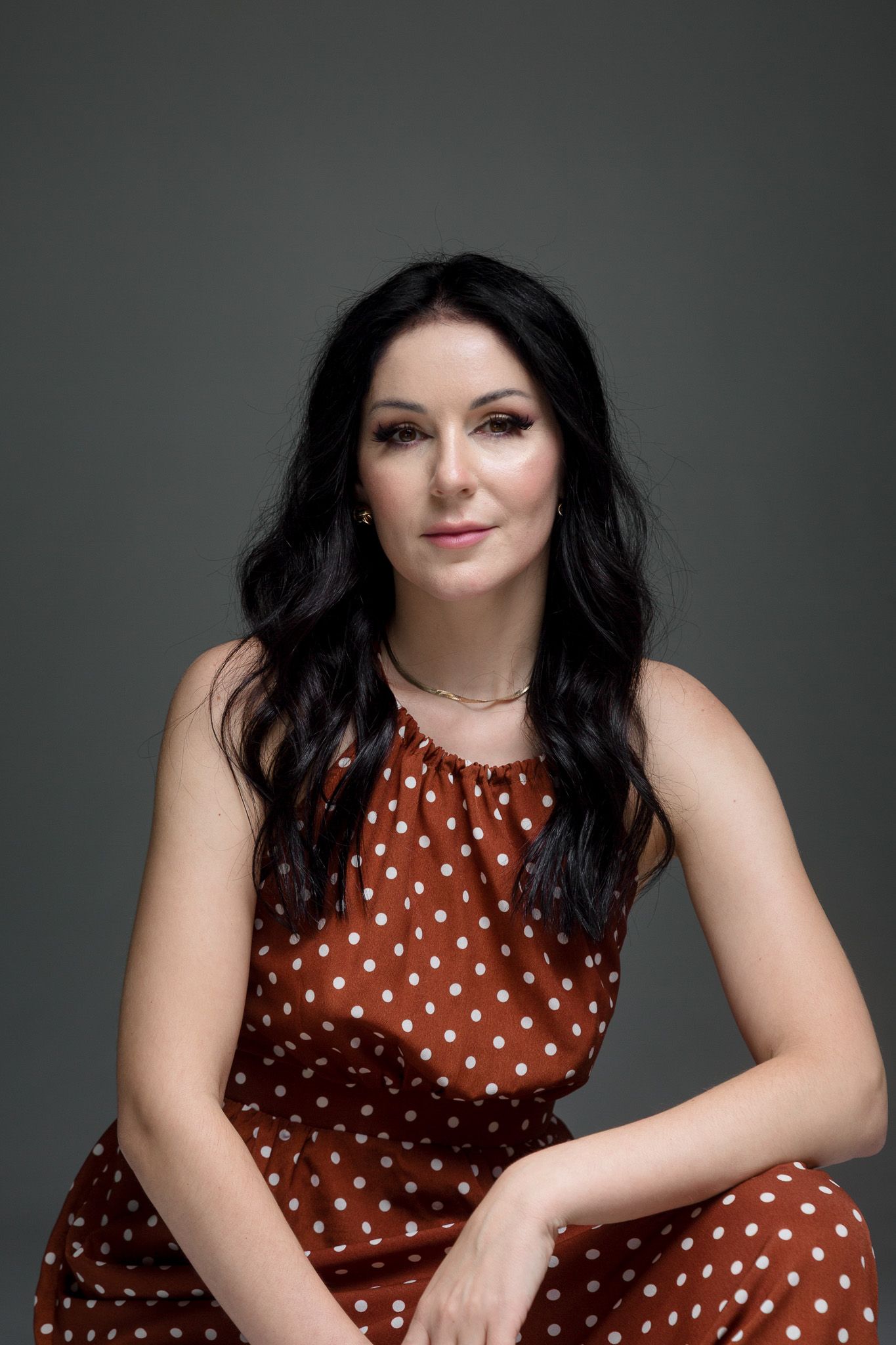 Professional studio portrait series in brown polka dot dress against dark background.