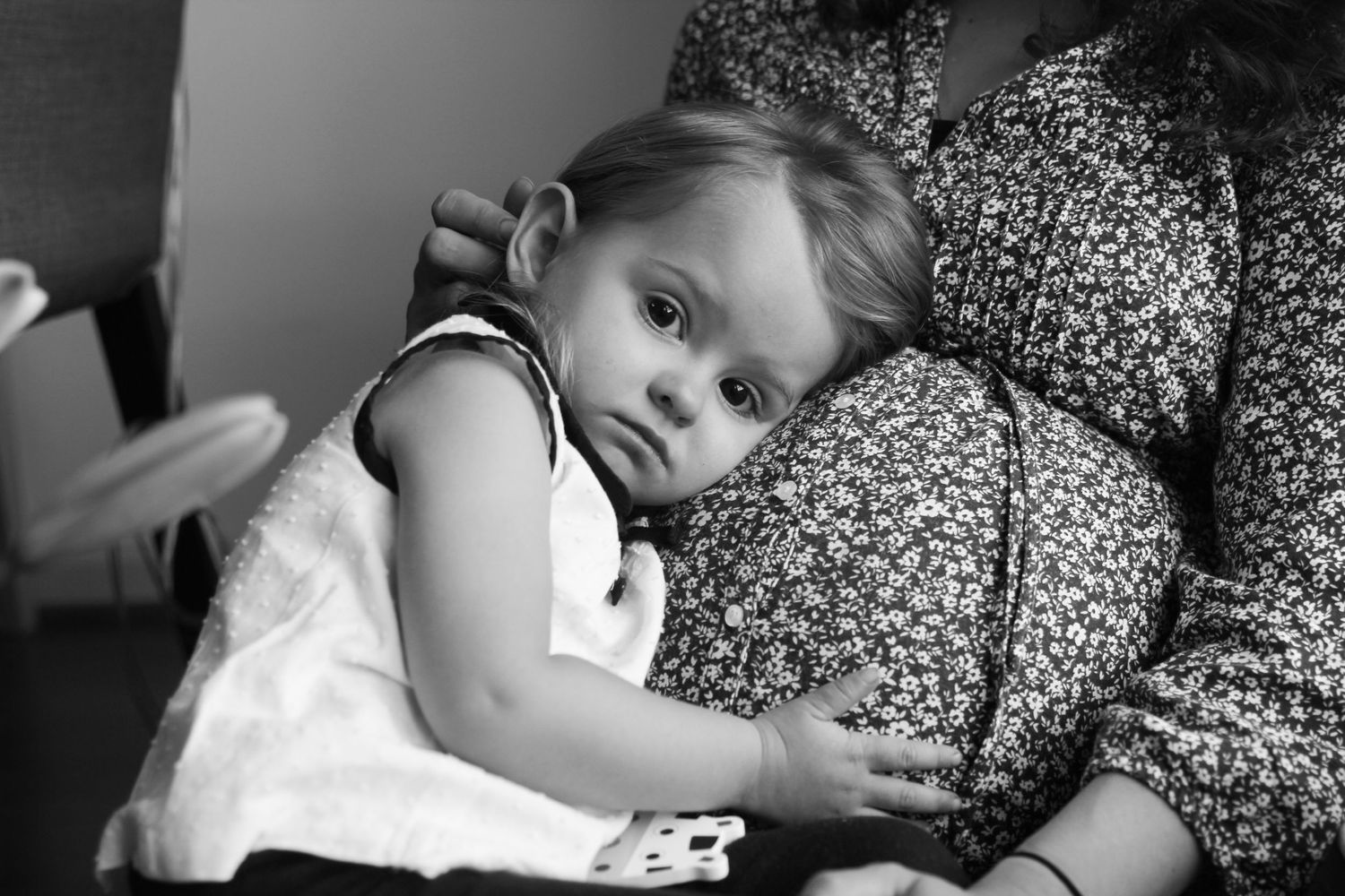 Black and white photo of a baby resting on an adult's lap, looking curiously at the camera.