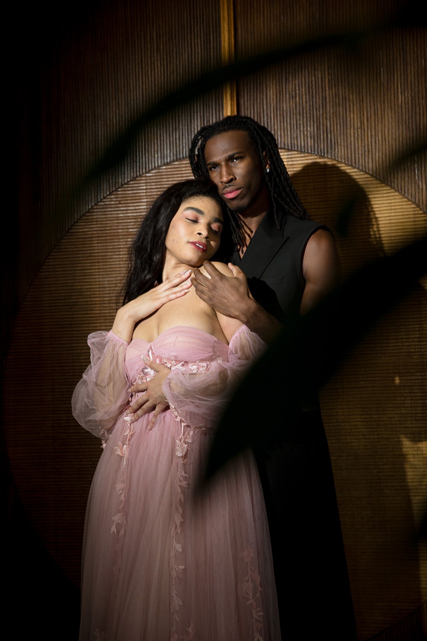 A romantic portrait of a couple embracing in soft lighting, with the woman wearing a delicate pink tulle gown.
