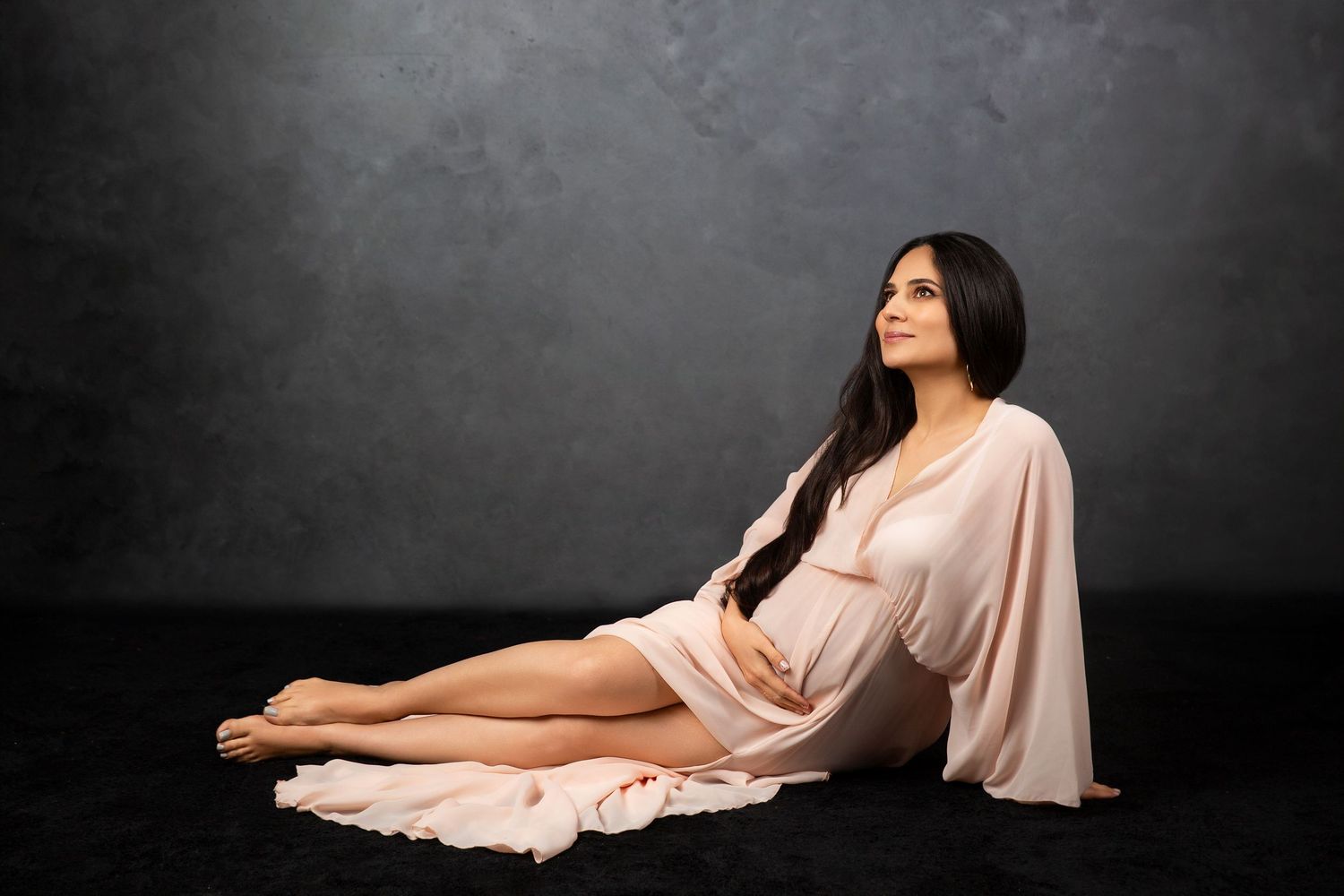 Artistic maternity photo with flowing peach dress in reclining pose.