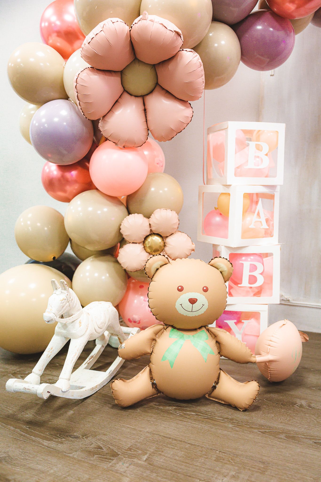 Baby shower decorations featuring balloon flowers, blocks spelling BABY, a rocking horse and teddy bear.
