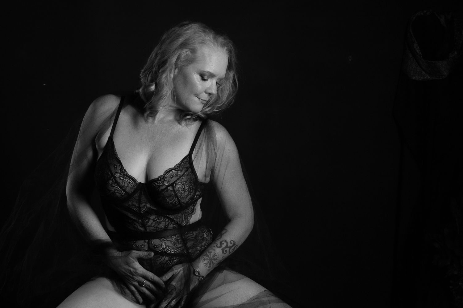 Artistic black and white boudoir photography featuring soft lighting and lace lingerie against dark background.