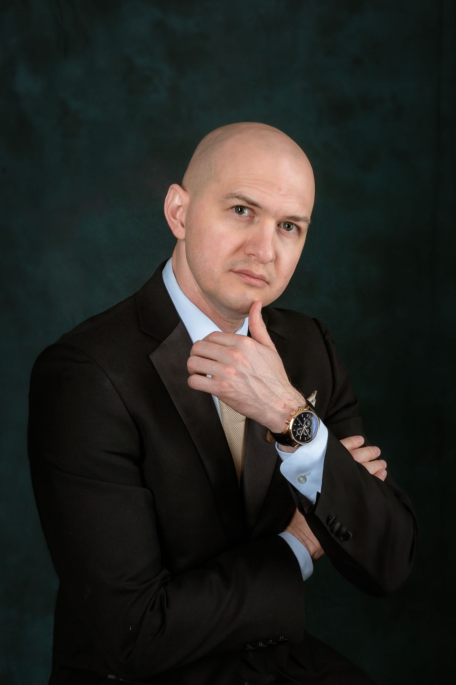 Professional headshot series in black suit against dark background.