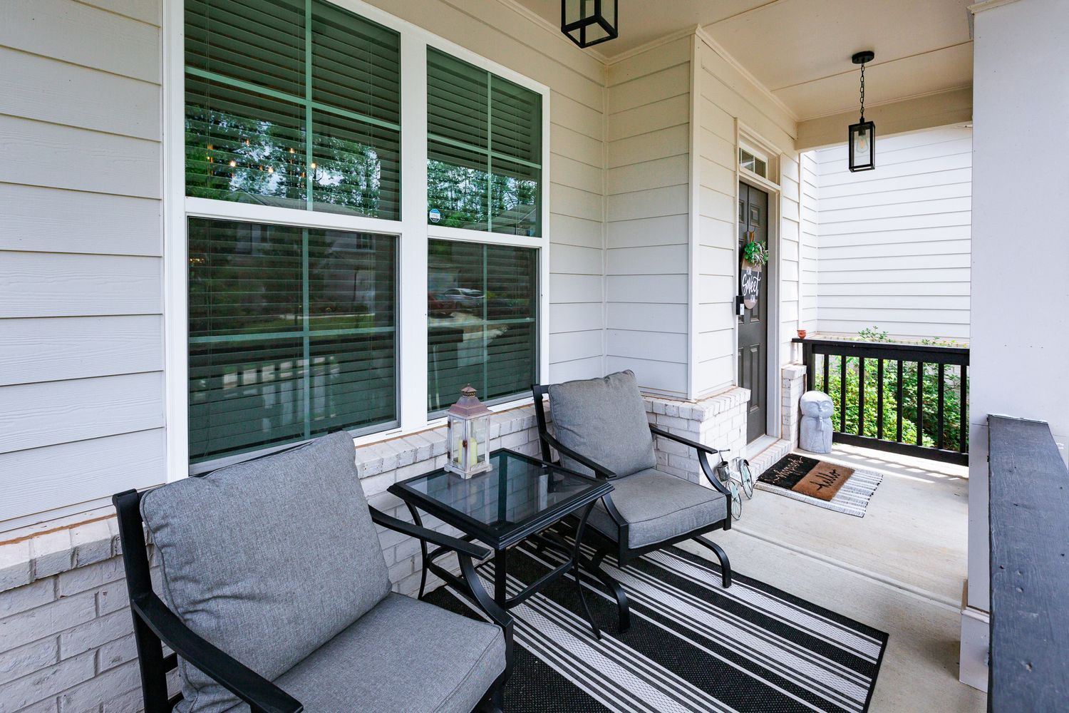 Modern porch seating area with grey cushioned furniture and glass table on striped outdoor rug.