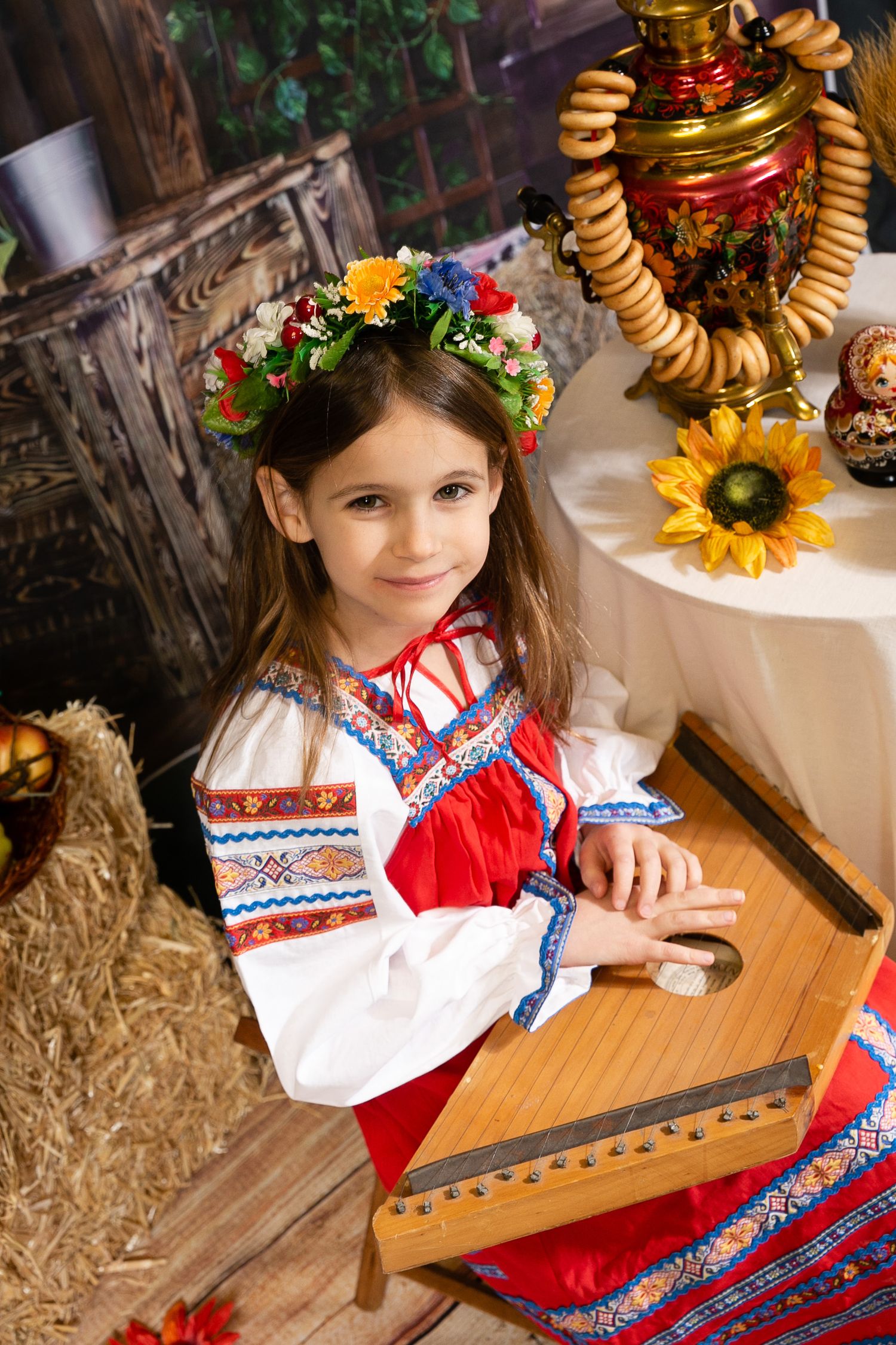 Traditional folk costume and wooden musical instrument in rustic setting with sunflowers and decorative elements.