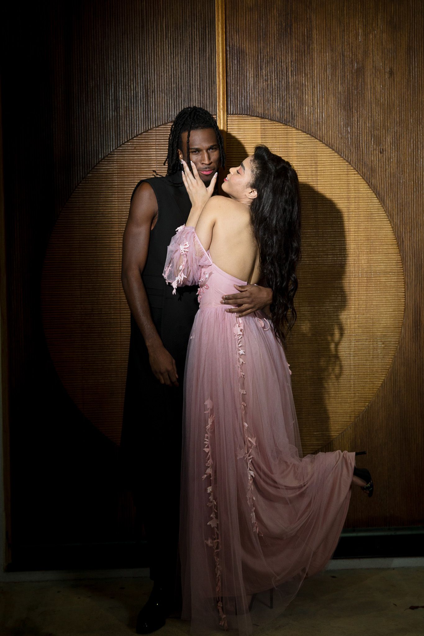 A romantic couple embraces against a wooden wall with dramatic lighting creating a circular spotlight effect behind them.