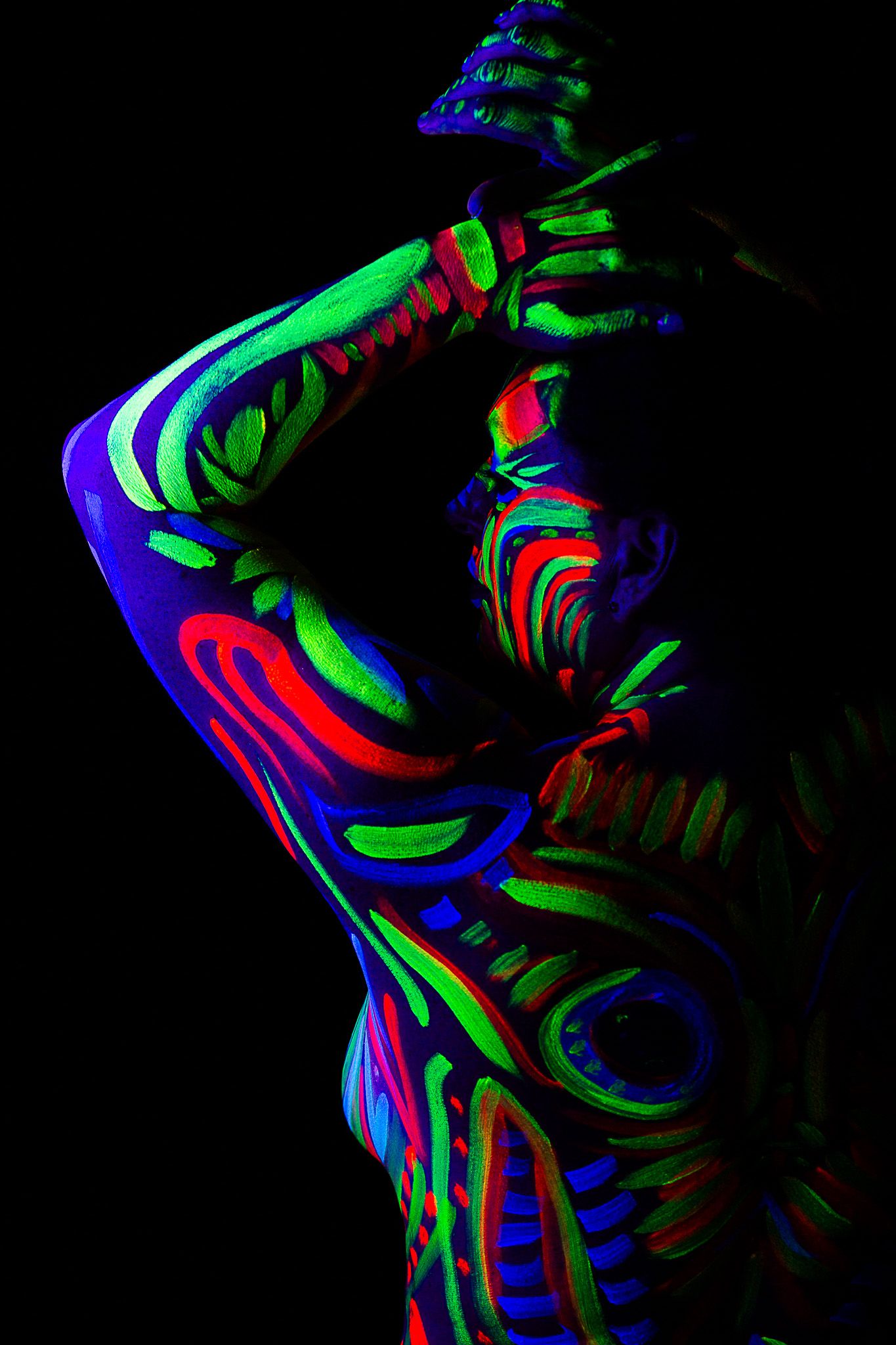 Artistic nude covered in swirling neon body paint patterns under blacklight.