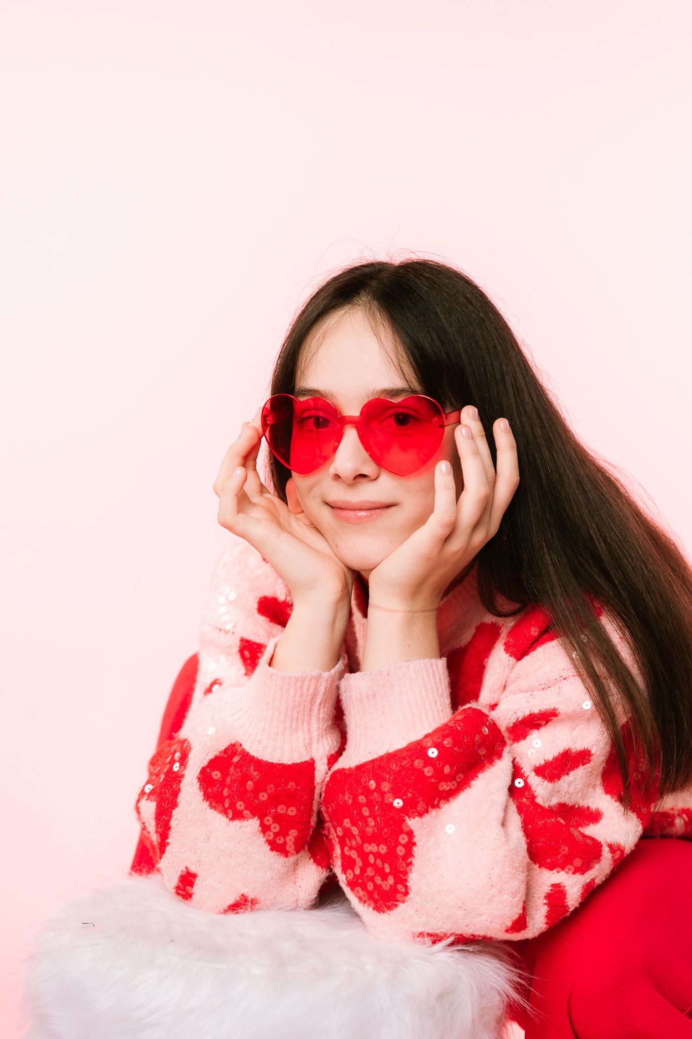 Stylish Valentine's portrait with red heart sunglasses and patterned sweater against pink background.