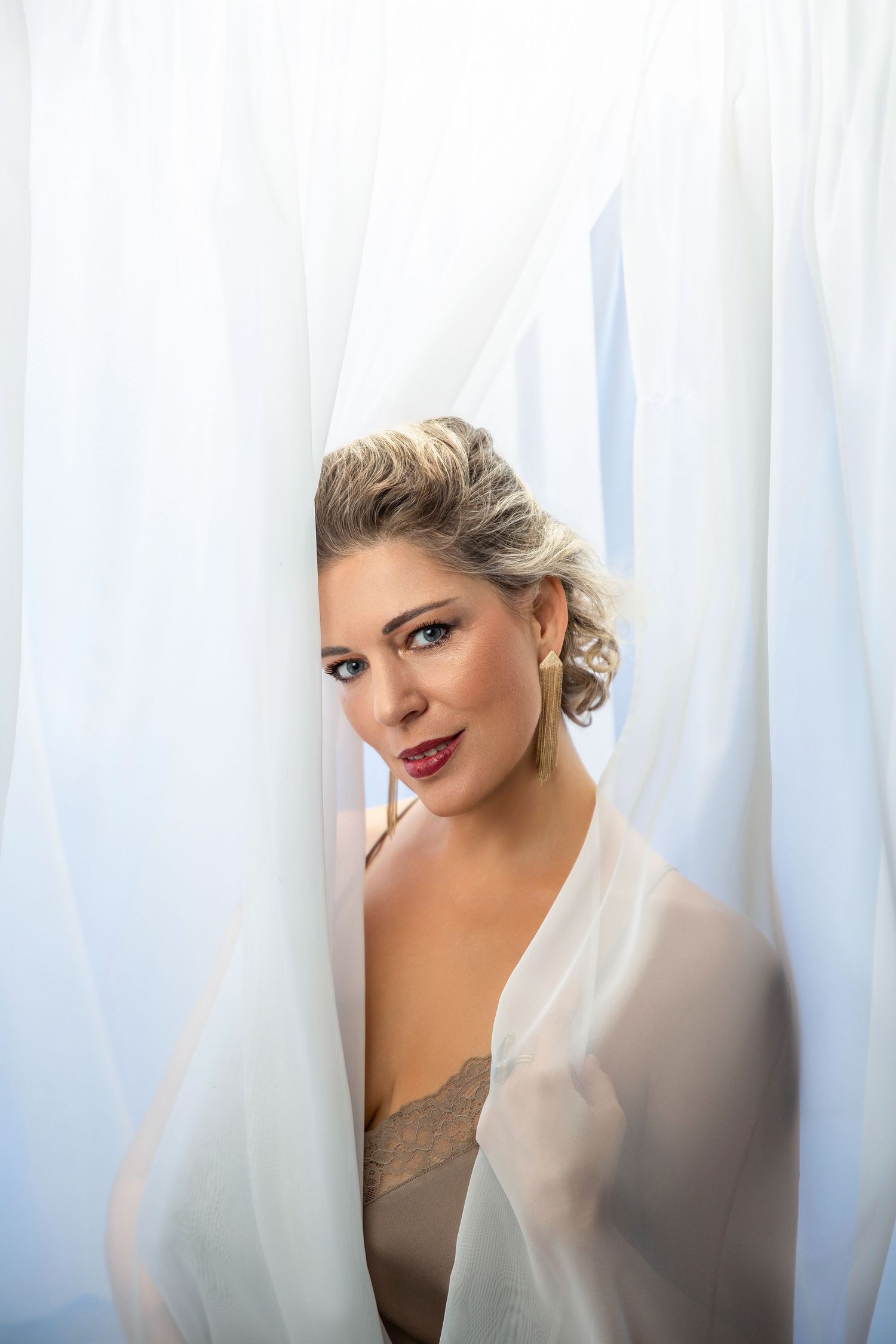 Elegant portrait through sheer white curtains in soft lighting.