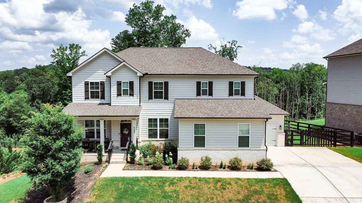 Aerial view of a white residential house with a spacious backyard and driveway surrounded by trees.