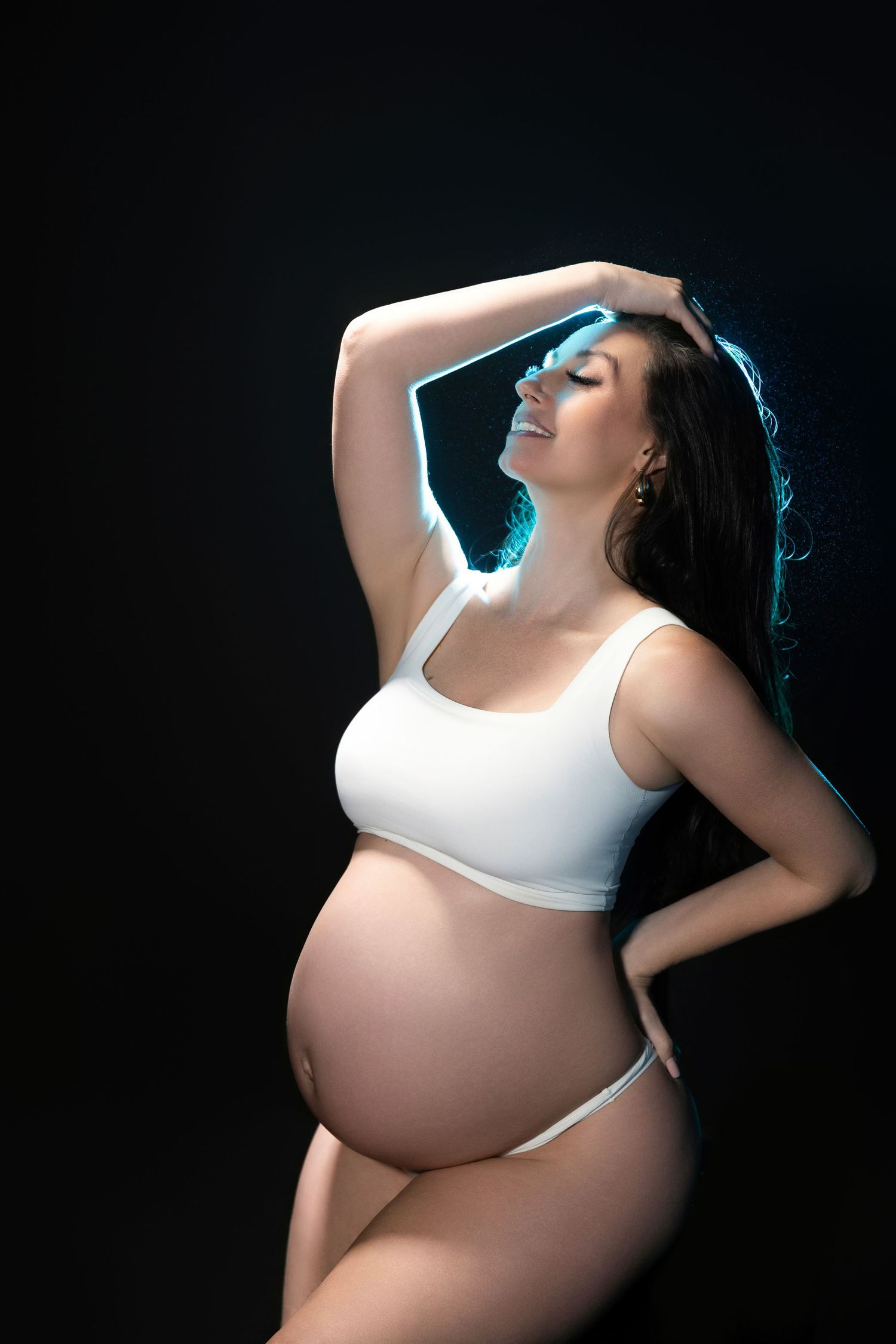 Dramatic side-lit maternity portraits in white top against dark background.