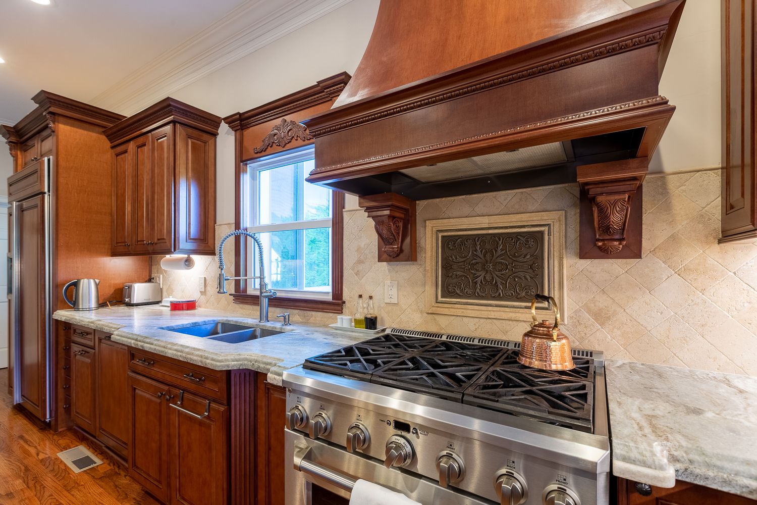 Professional grade kitchen with stainless appliances, marble backsplash and decorative wood corbels.