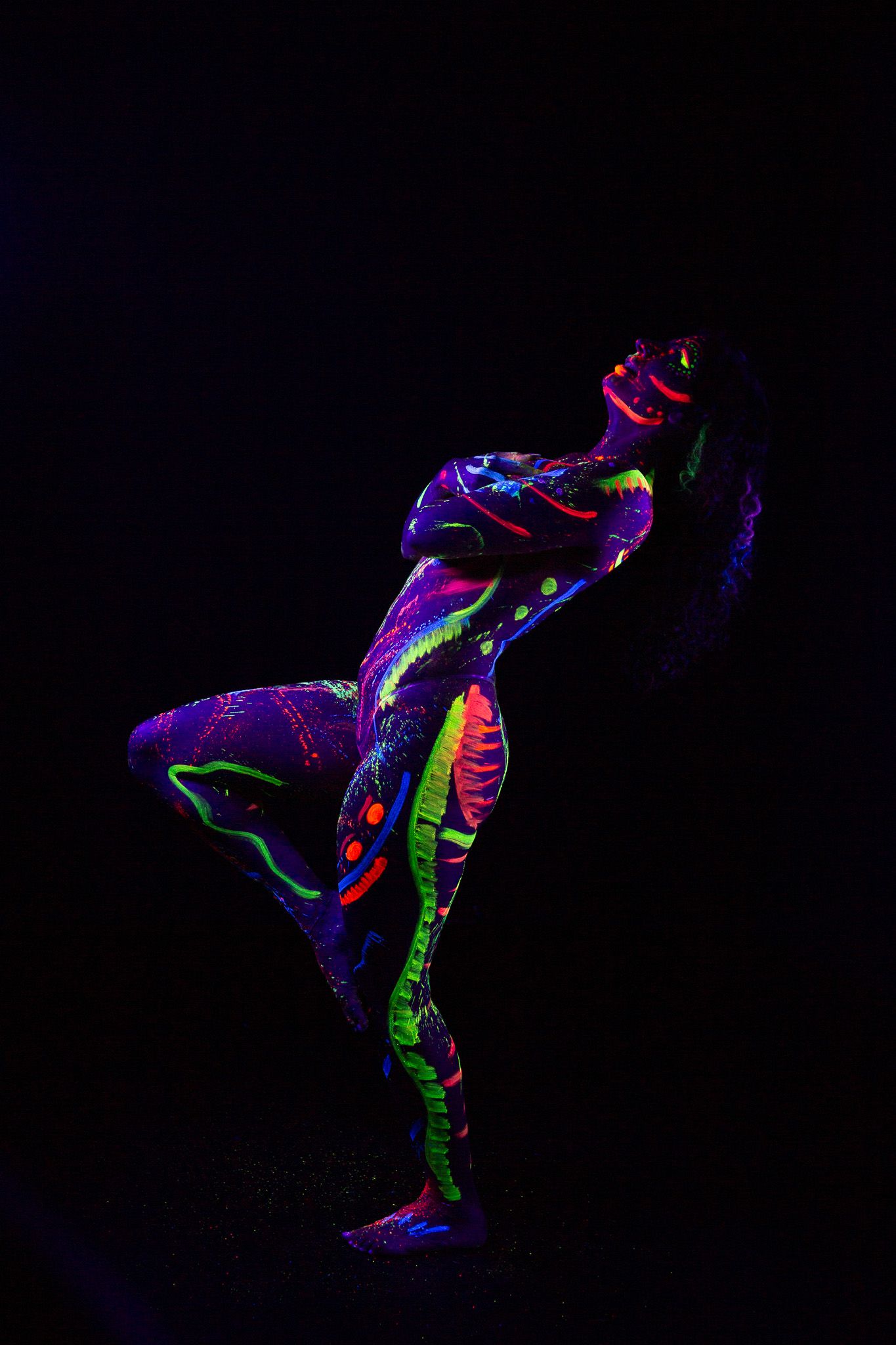 Dancer in neon body paint striking dynamic pose against black background.