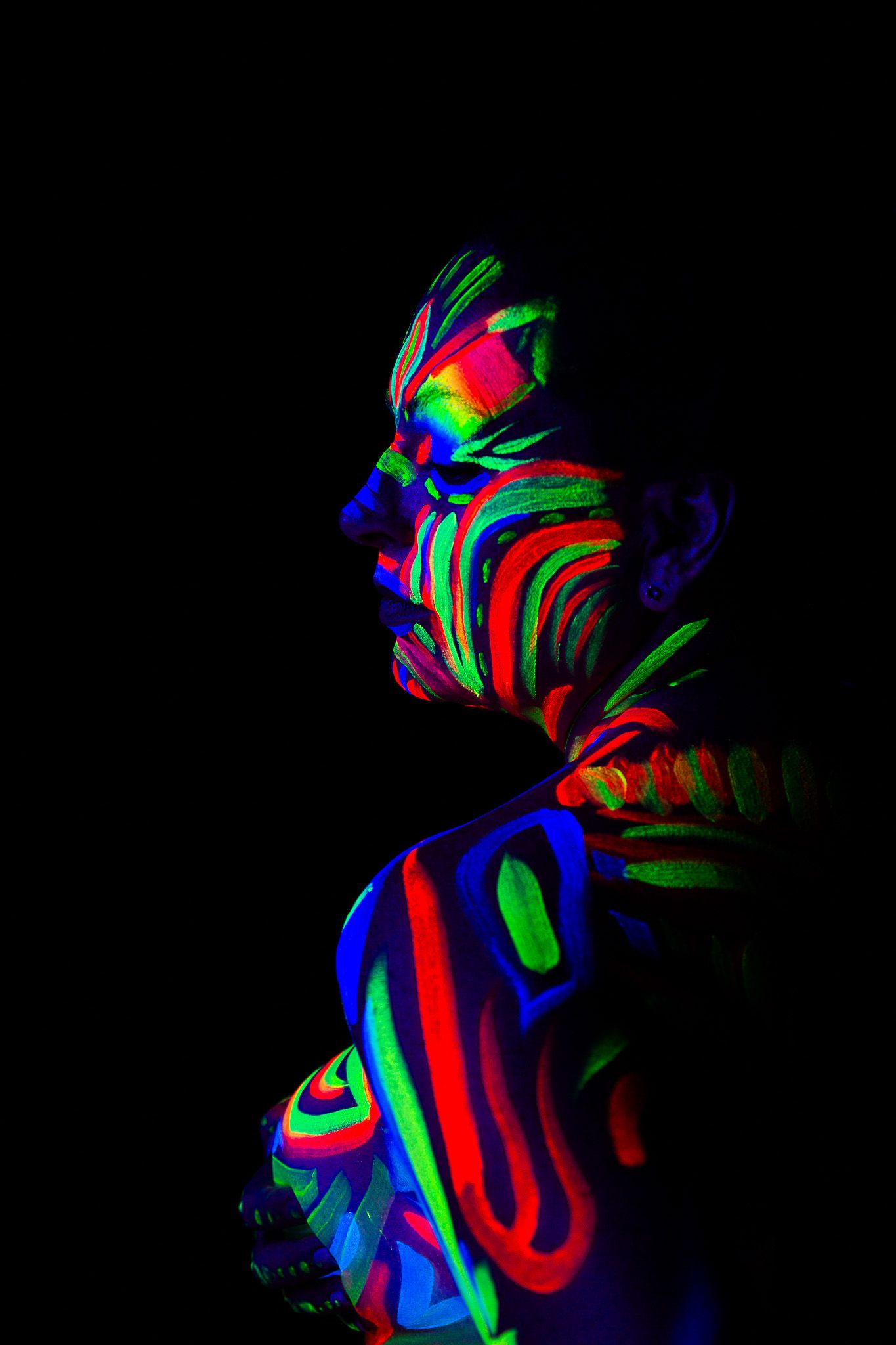 Profile view of figure decorated with fluorescent body paint creating abstract patterns.