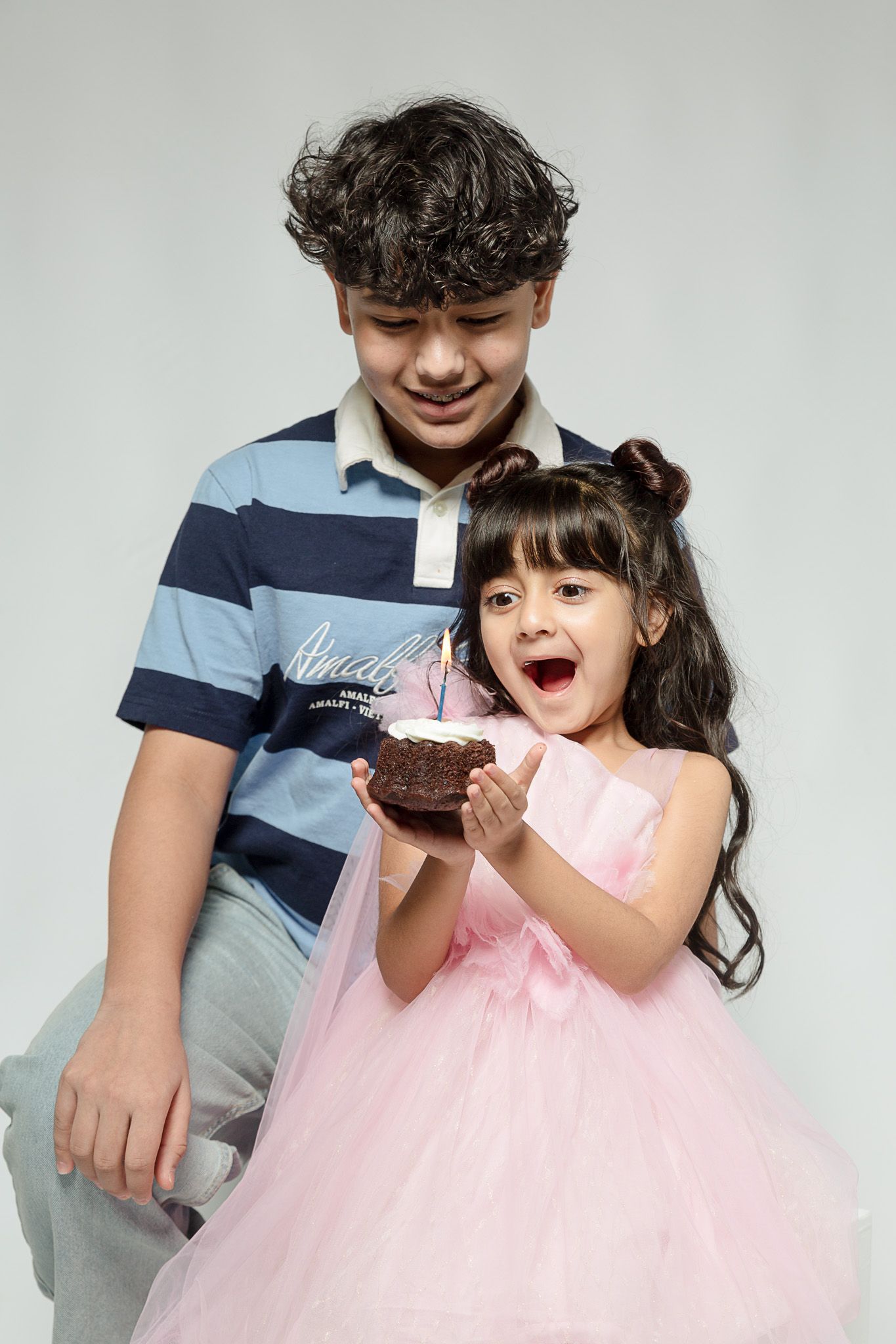 A boy and little girl in a pink dress celebrating her birthday with a small chocolate cake with a candle.