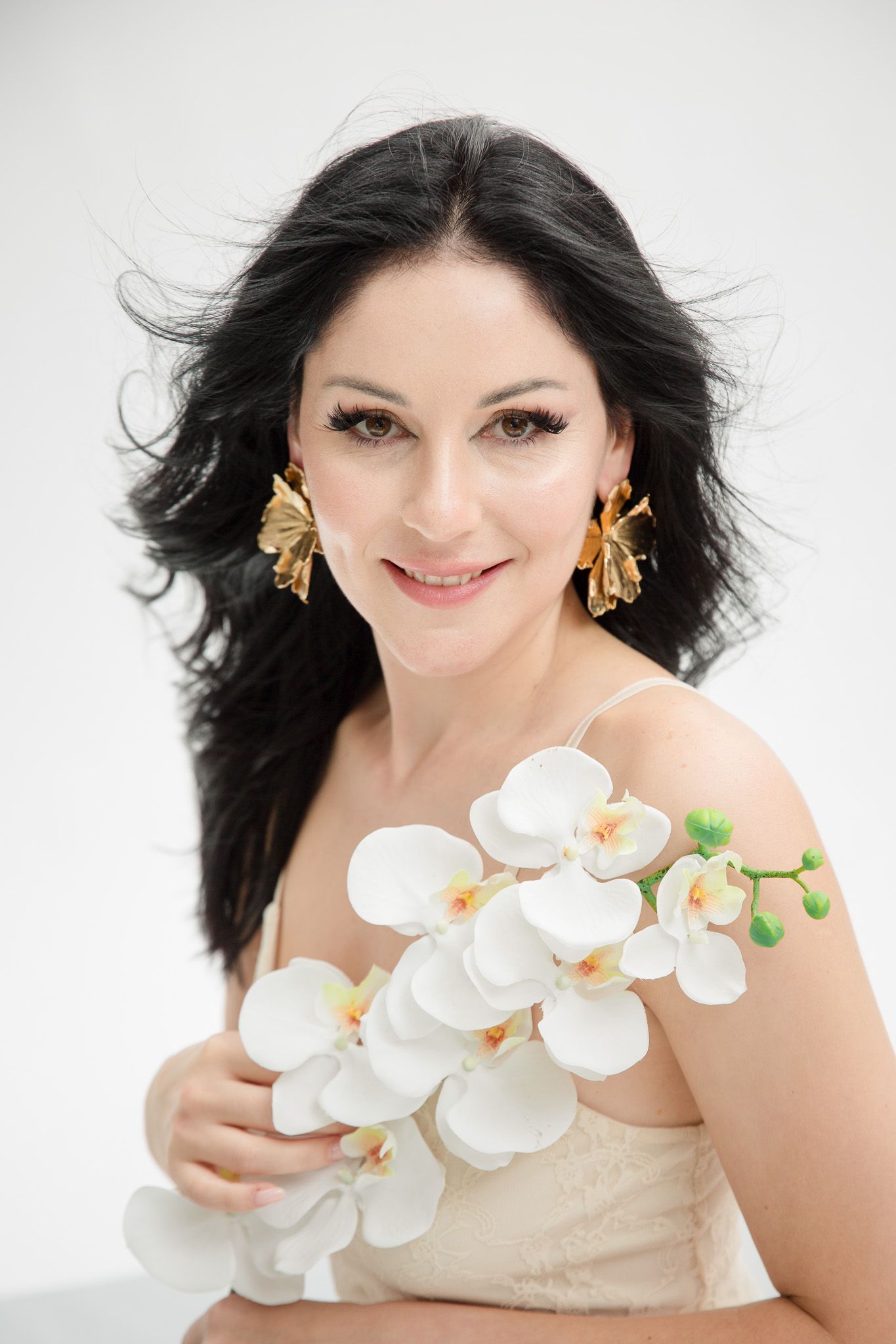 Glamour portrait with white orchids and gold butterfly earrings against white backdrop.